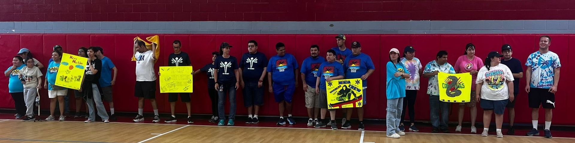 People holding signs on a basketball court in front of a red wall.