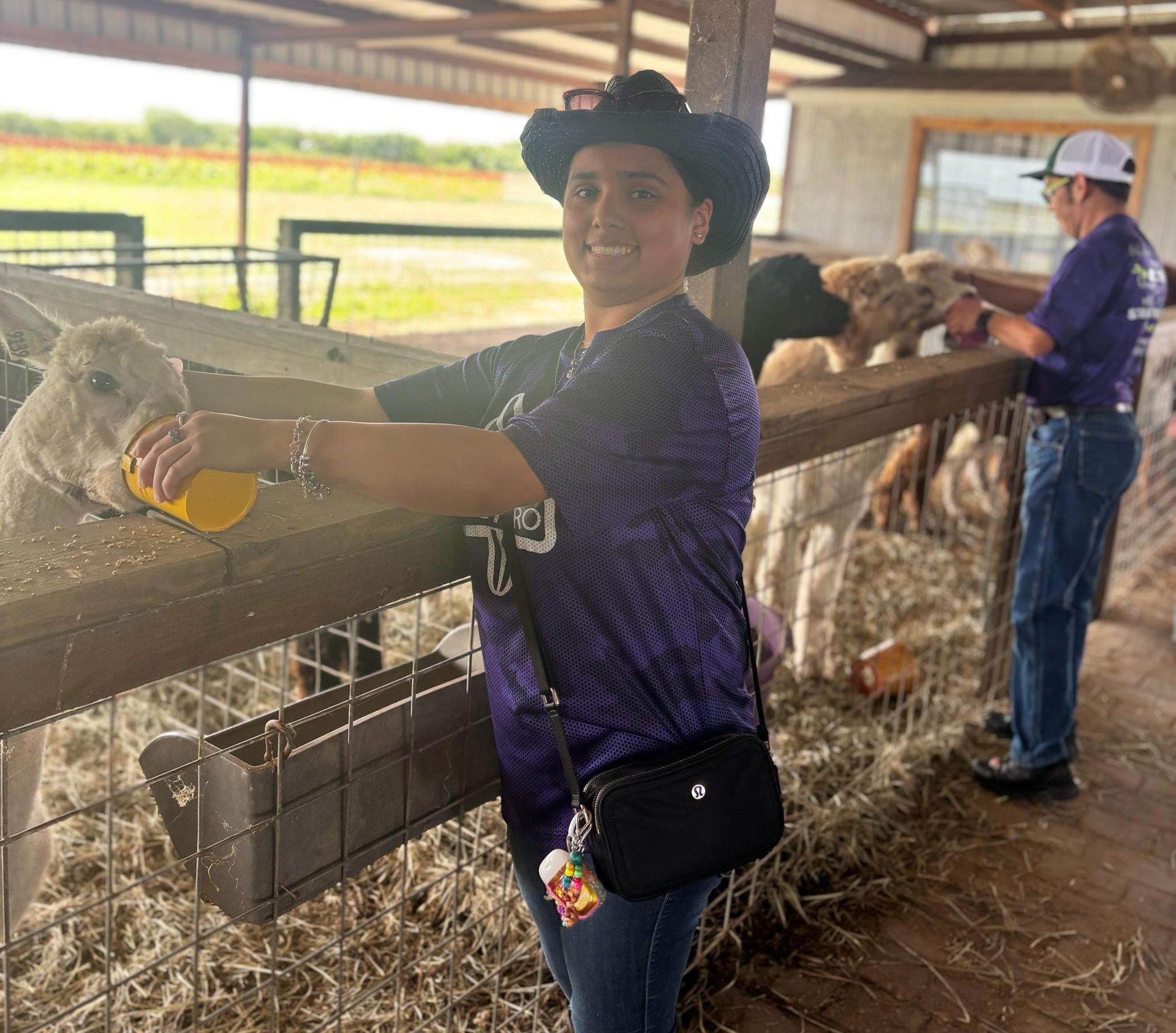 Woman in a cowboy hat pets a fluffy cow at a farm, another person is in the background.