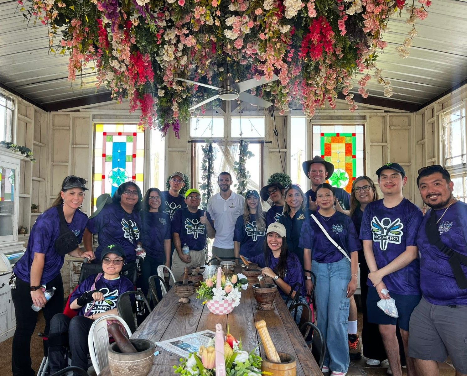Group of people in purple shirts around a wooden table under a floral ceiling.