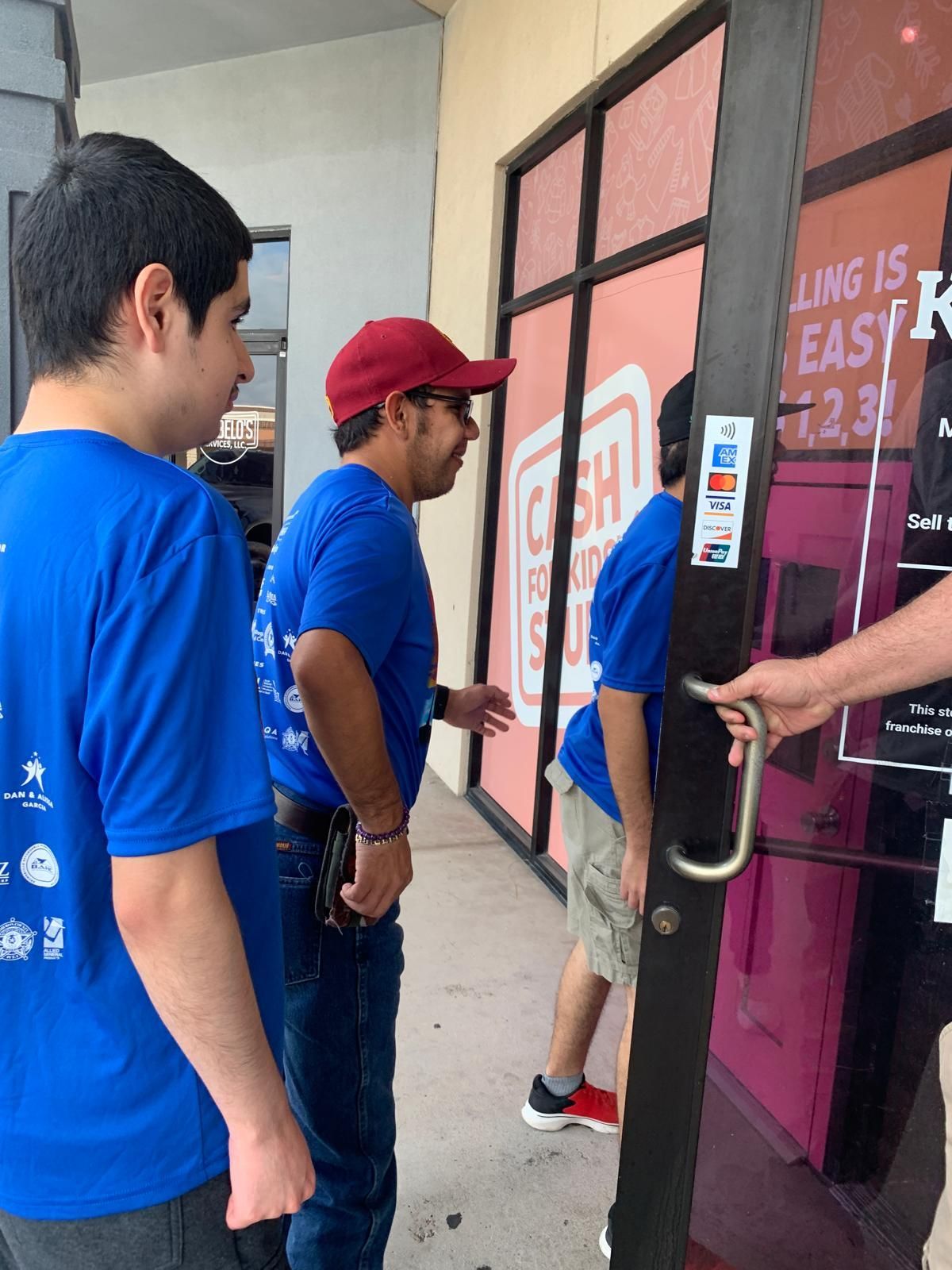 Three men in blue shirts and a man in a red hat attempt to enter a store with pink signage.
