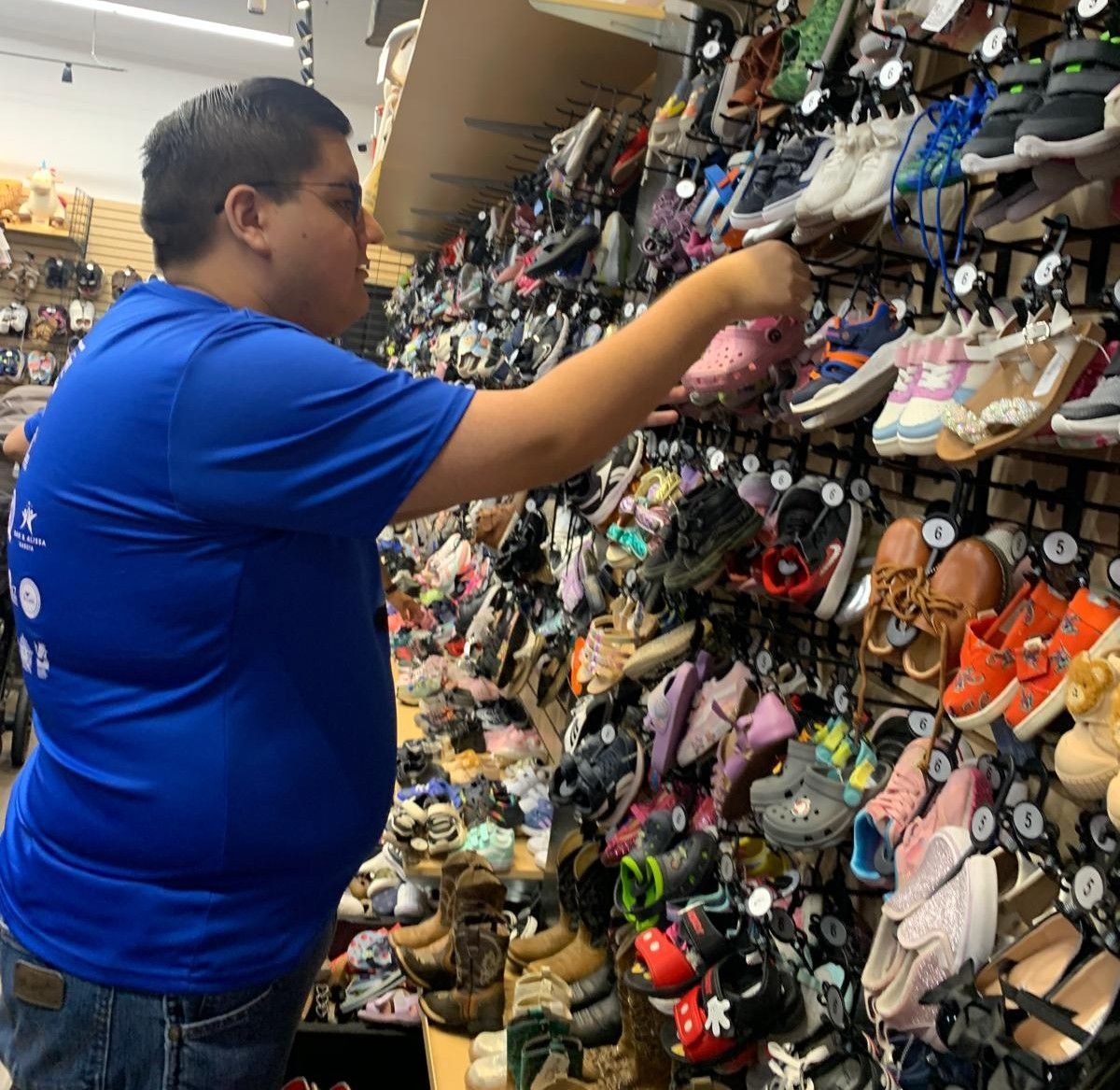 Man in blue shirt reaching for shoes on a wall display in a store.