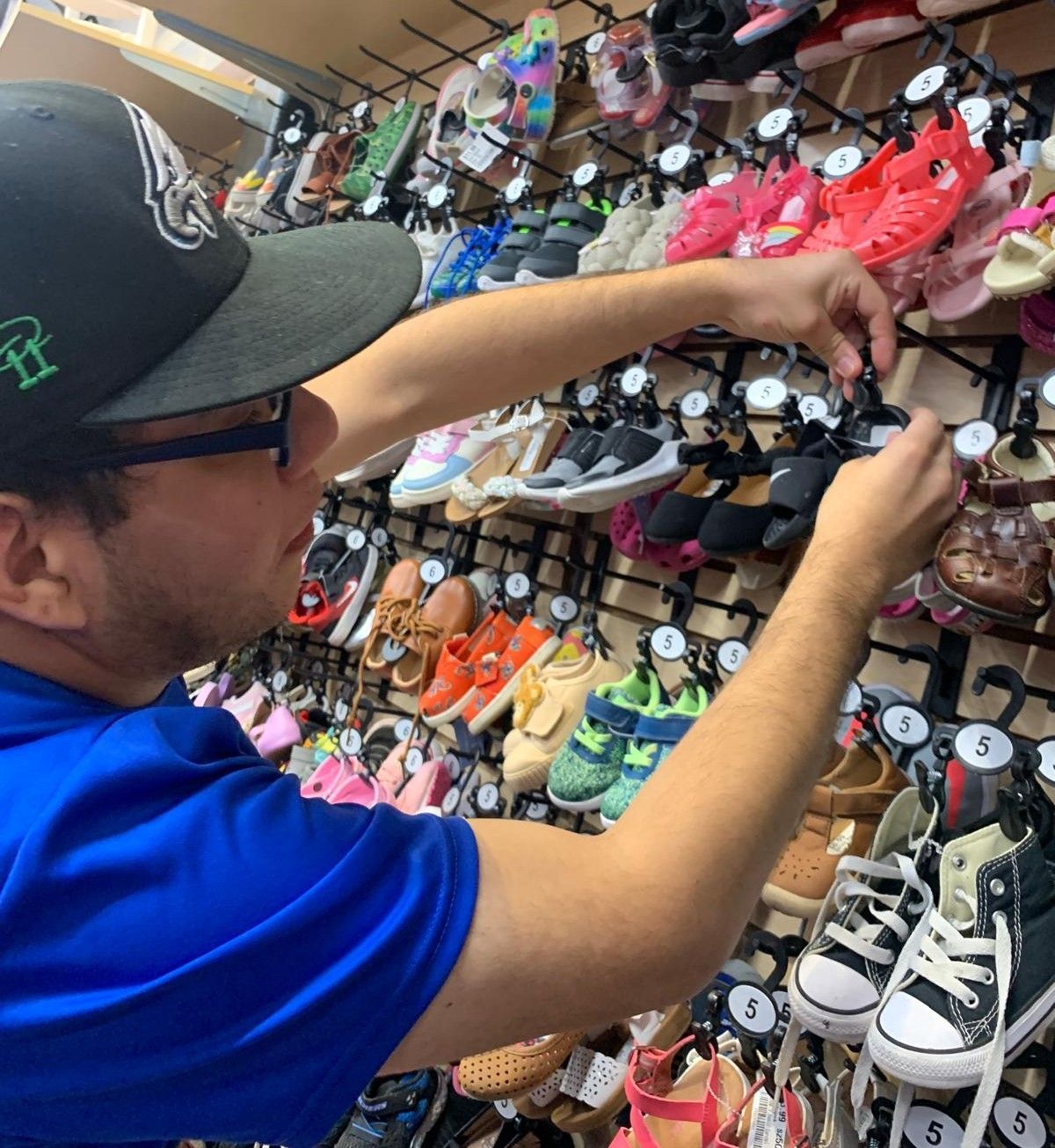Man arranging shoes on a display rack in a store.
