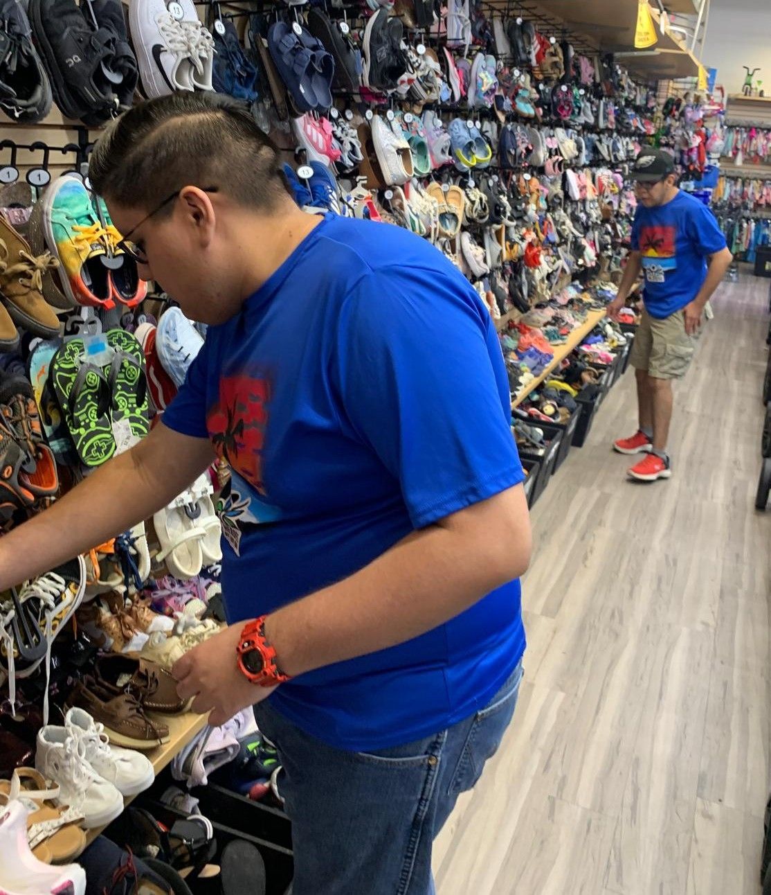 Two people browsing shoes in a shop. One is selecting shoes. Shelves of shoes line the walls.