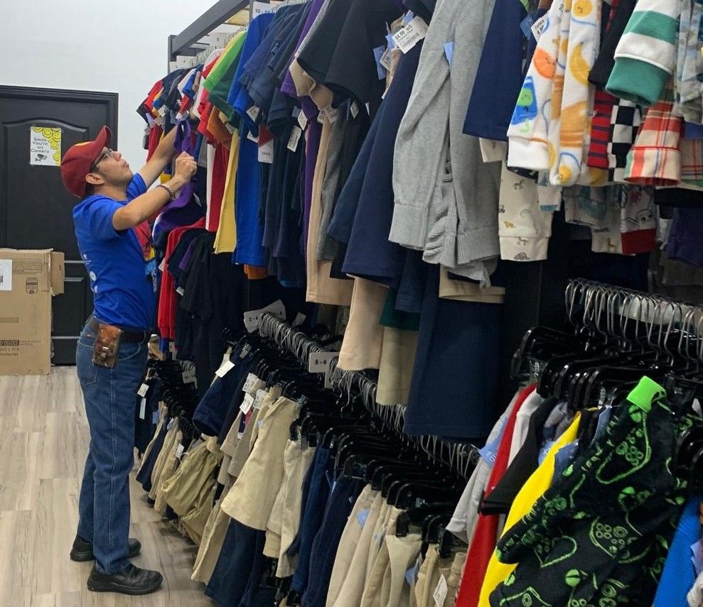 A person in a blue shirt and red cap is organizing clothes on a rack inside a store.