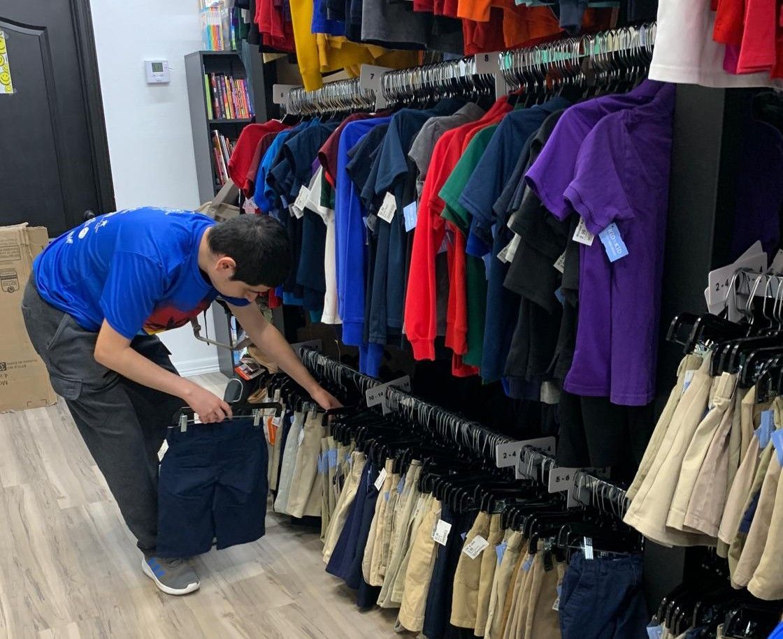 Person in a blue shirt selecting pants from a clothing rack in a store.