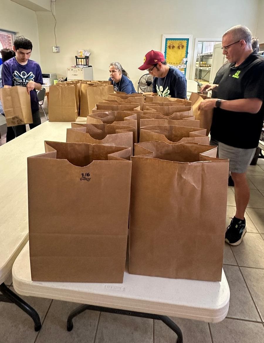 People packing brown paper bags on a table, likely for food distribution.