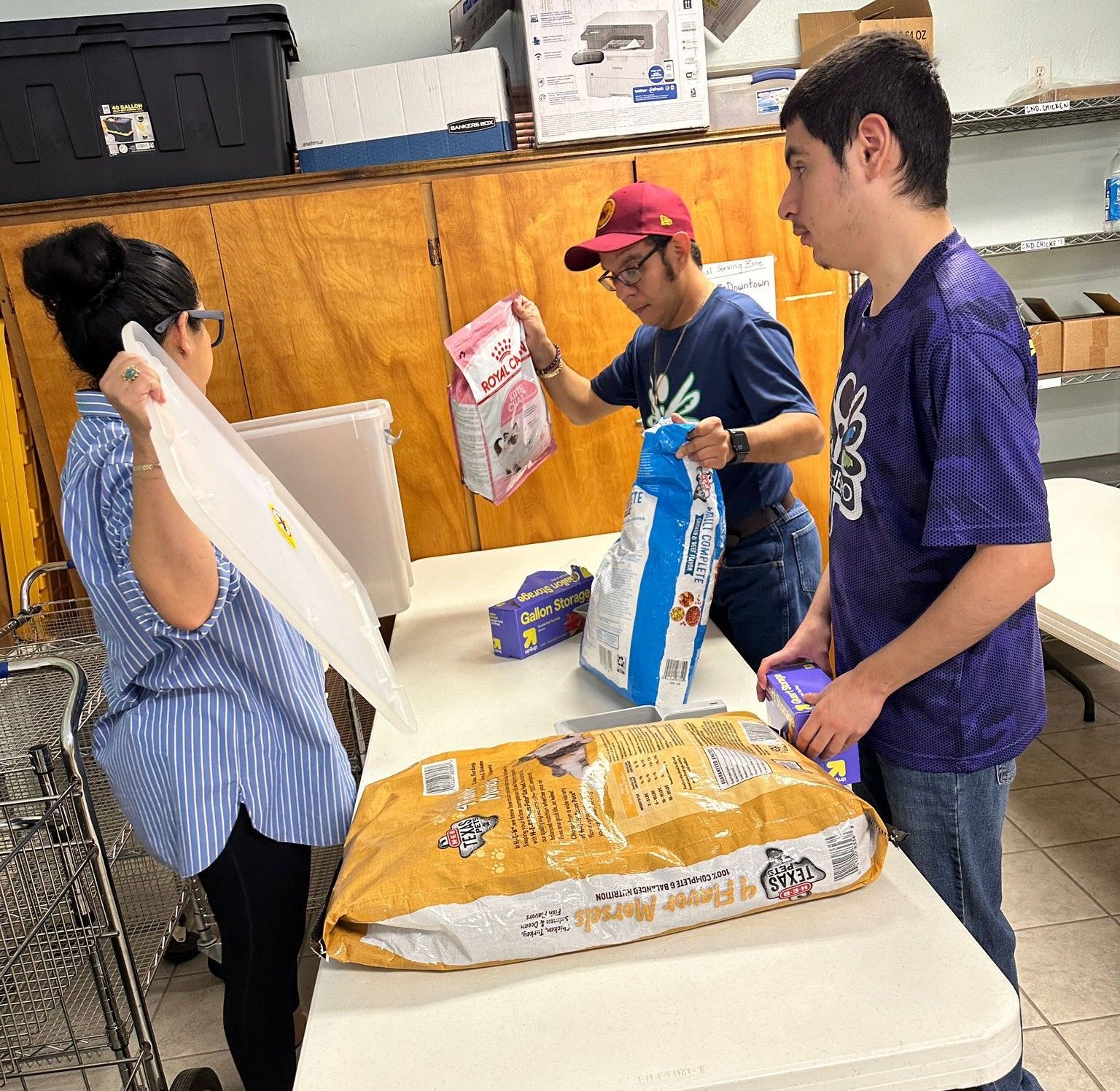 Three people packing pet food bags at a distribution center.