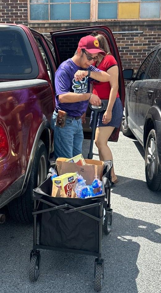 Man and woman unloading groceries from car into a wagon. Sunny day.