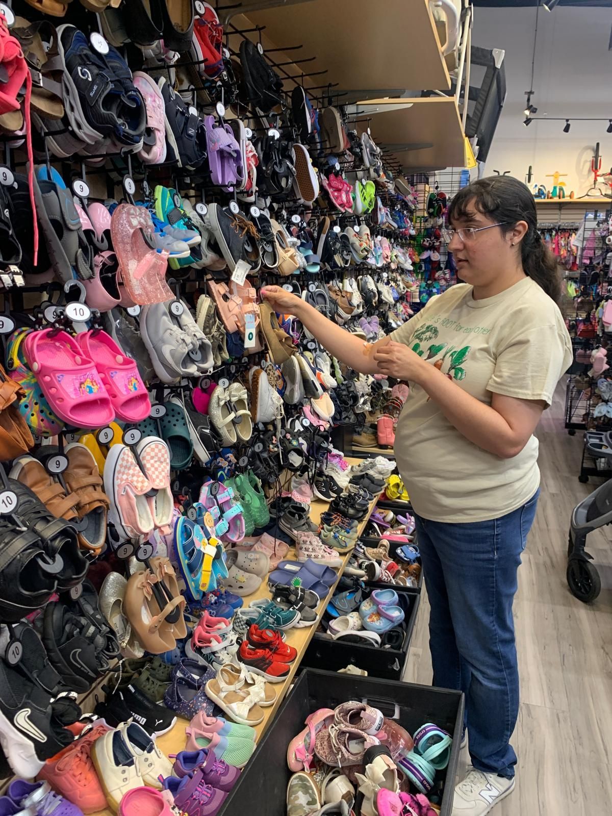 Woman in shoe store examines merchandise on a wall display, surrounded by numerous colorful shoes.