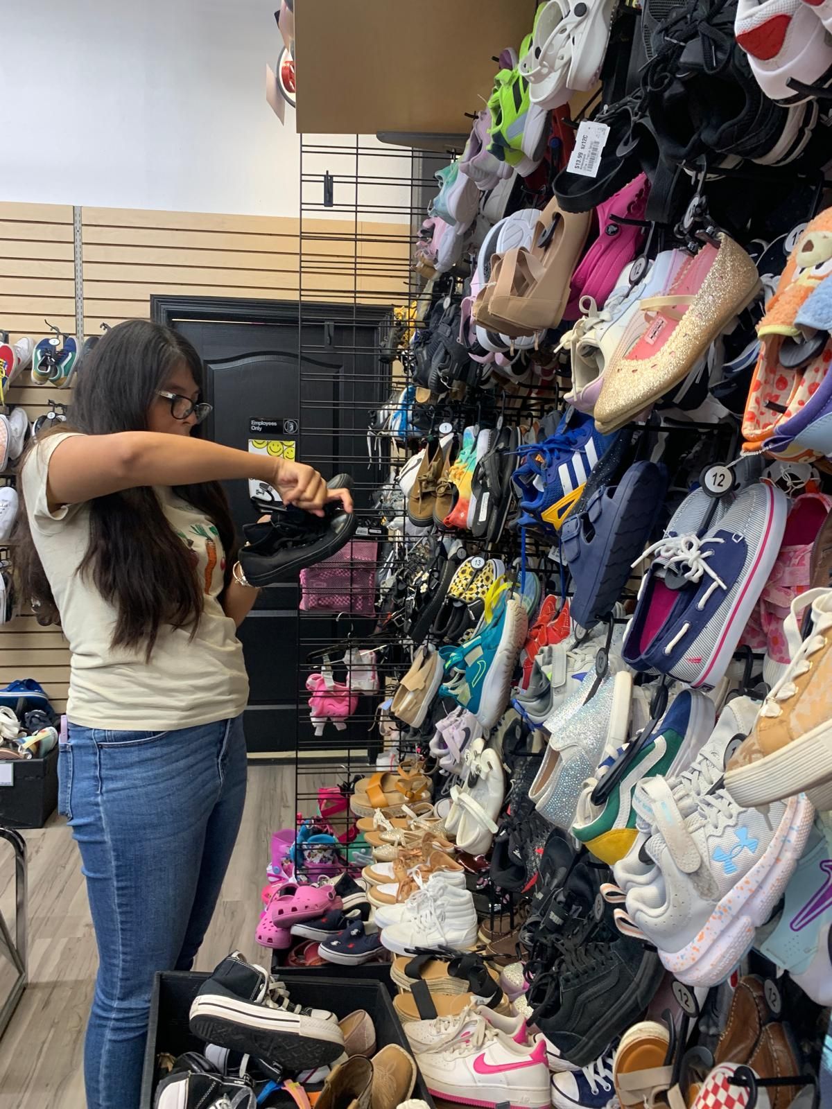 Woman in a shoe store looking at a black shoe, surrounded by a wall of colorful shoes.