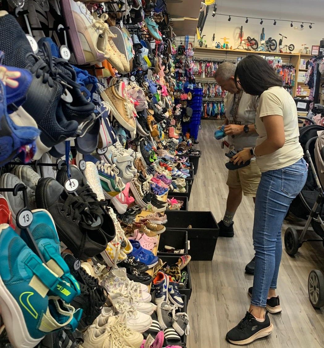 People shopping for shoes in a store. A wall displays many shoes, and shoppers browse them.