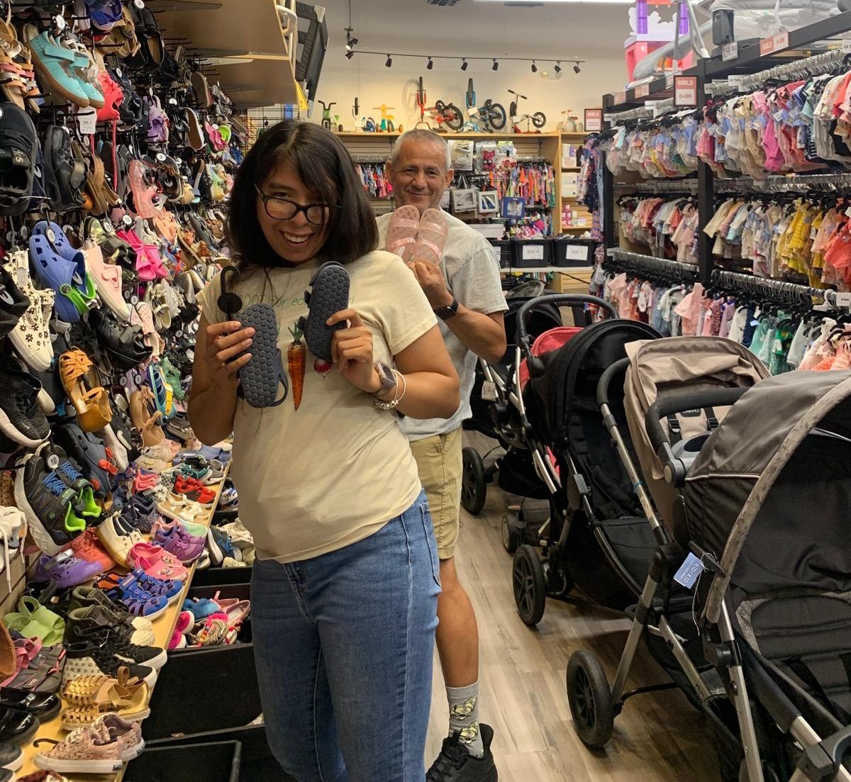 A woman and man in a shoe store hold up Crocs. They are smiling. Store has many shoes.