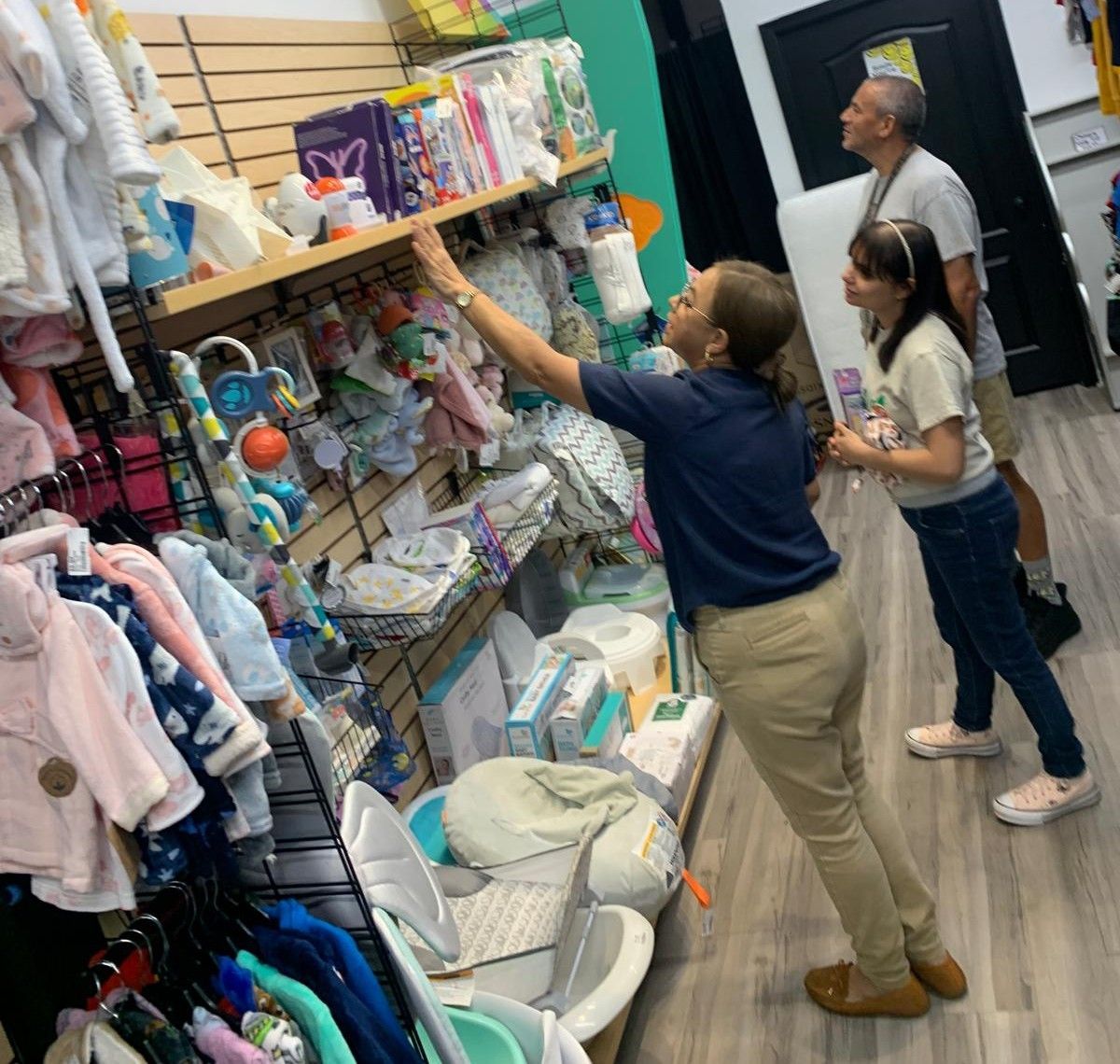 Woman reaching for item on shelf in store.  A man and girl look on.