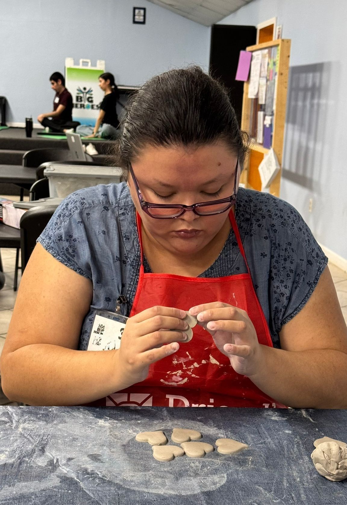 Woman in apron sculpting clay, focused, in a workshop setting.