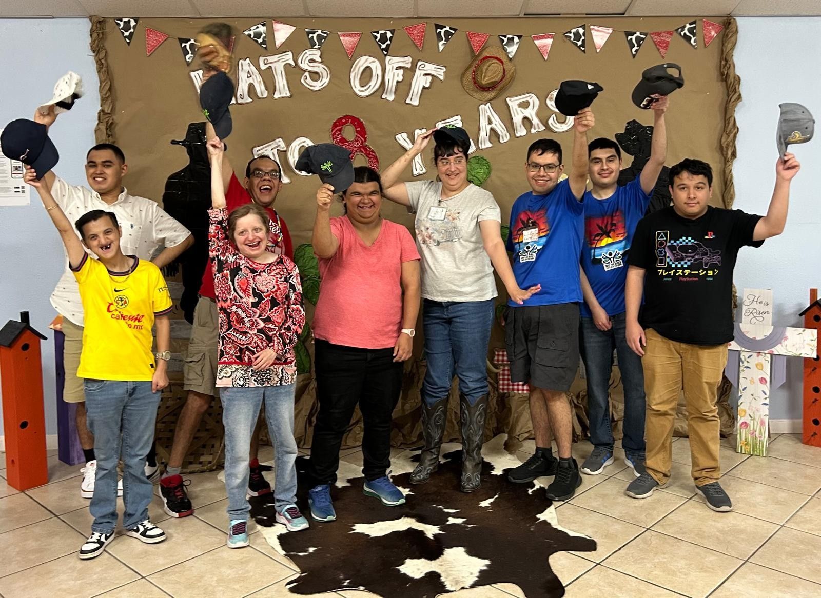 Group of people celebrating, raising hats. Western-themed backdrop.