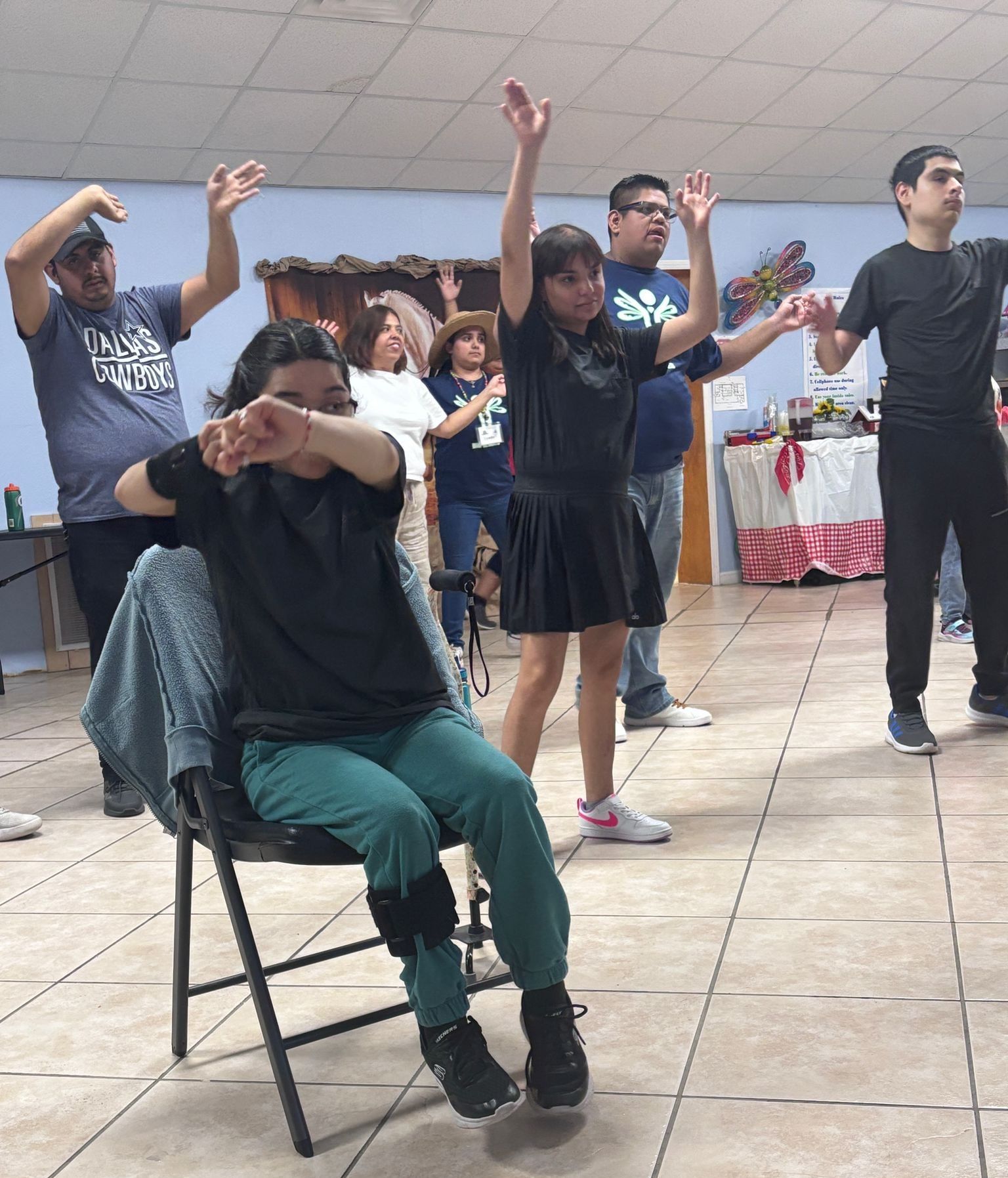 People with disabilities doing a dance class indoors. Some have arms raised; one is seated.
