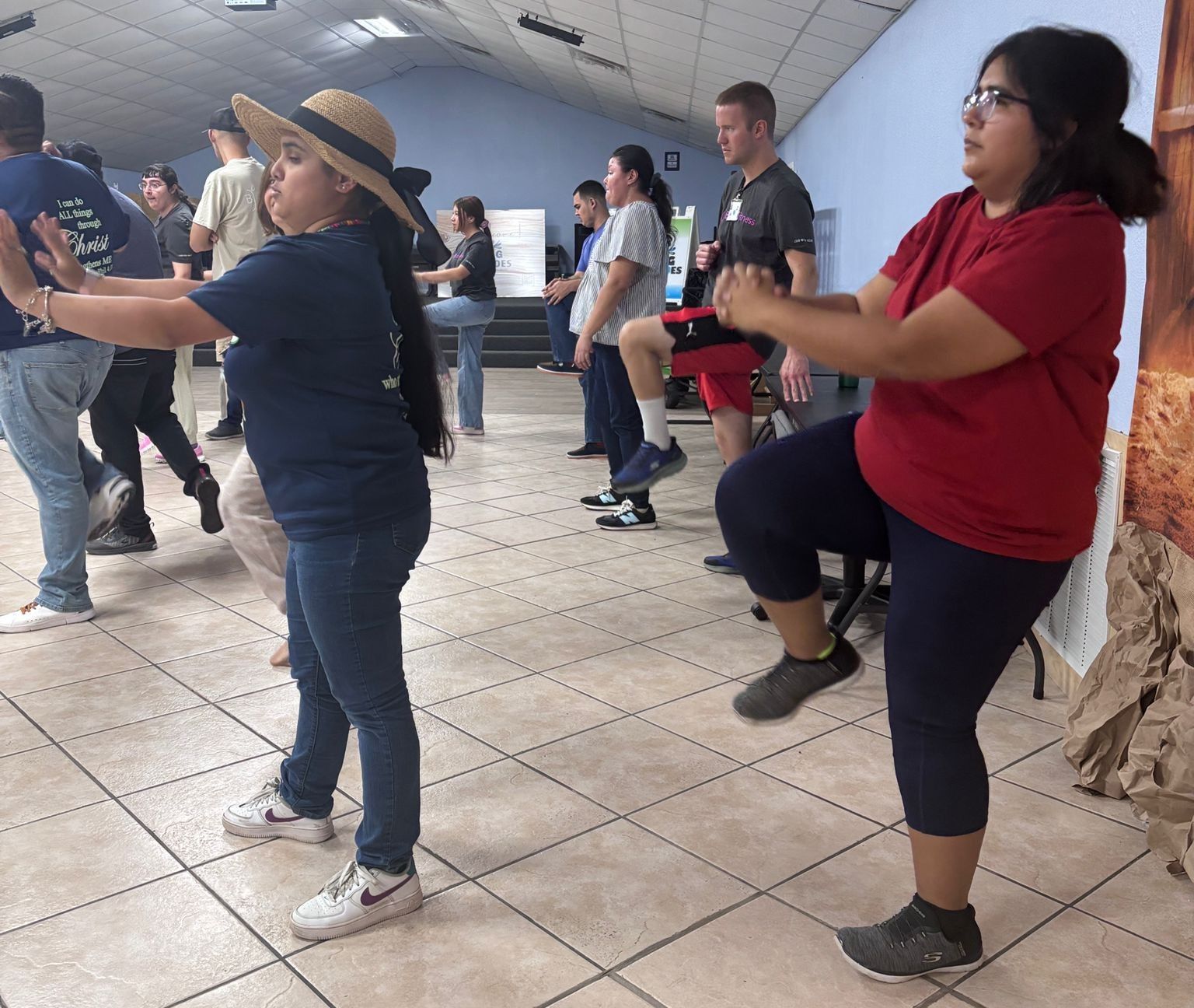 Group of people exercising indoors, doing leg lifts and arm stretches.