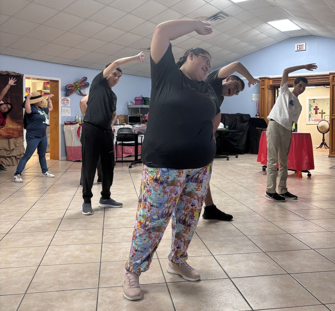 Group stretching indoors: diverse people in casual clothes, arms raised, bending.