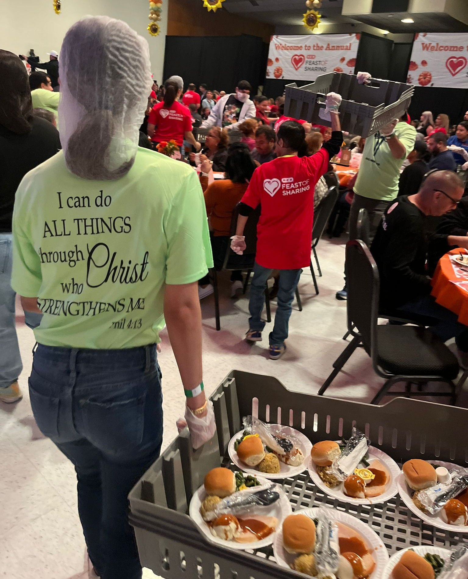 People serving food at a community event. Plates of food are in a serving tray.