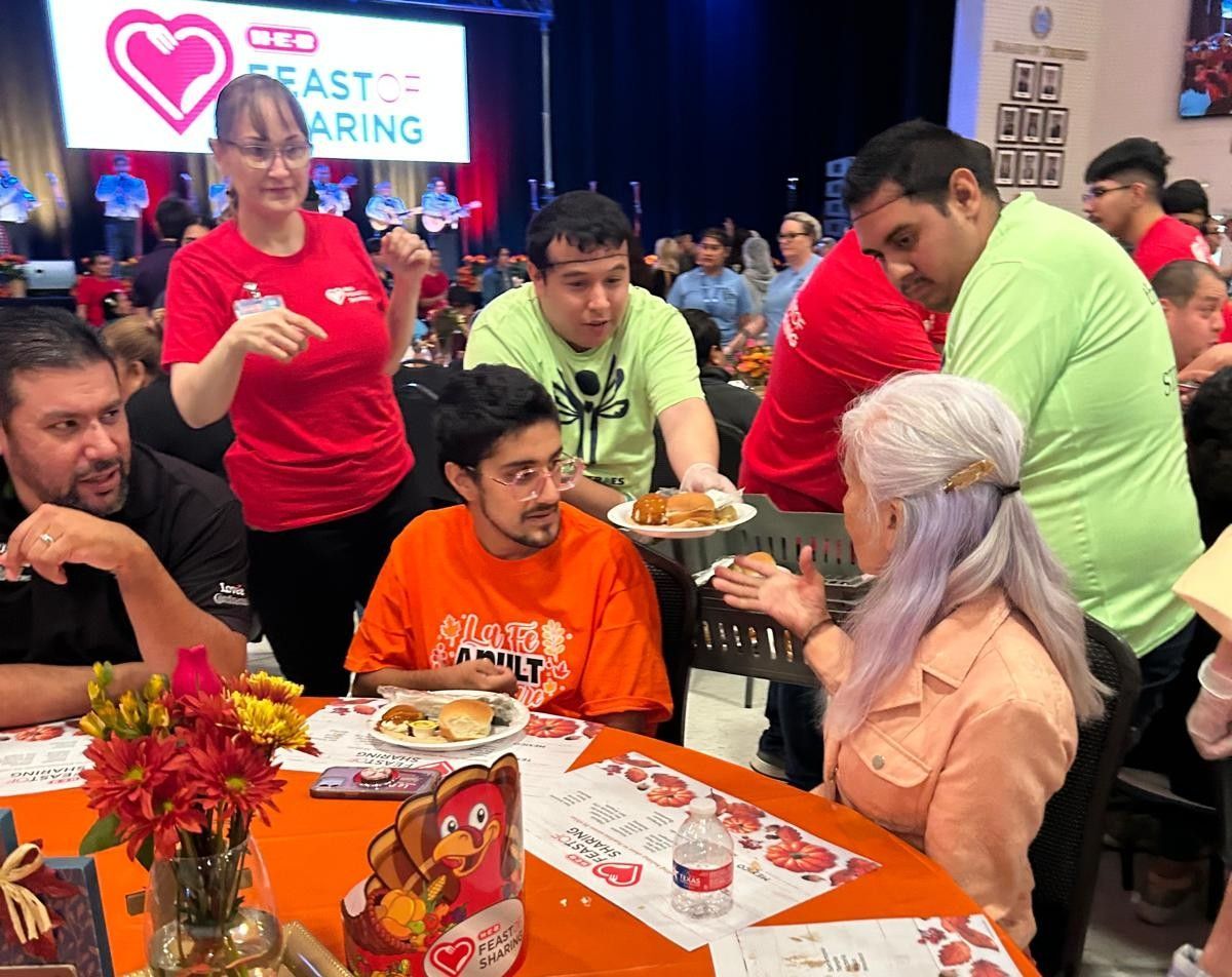 People served food at a dining table, event banner in the background.
