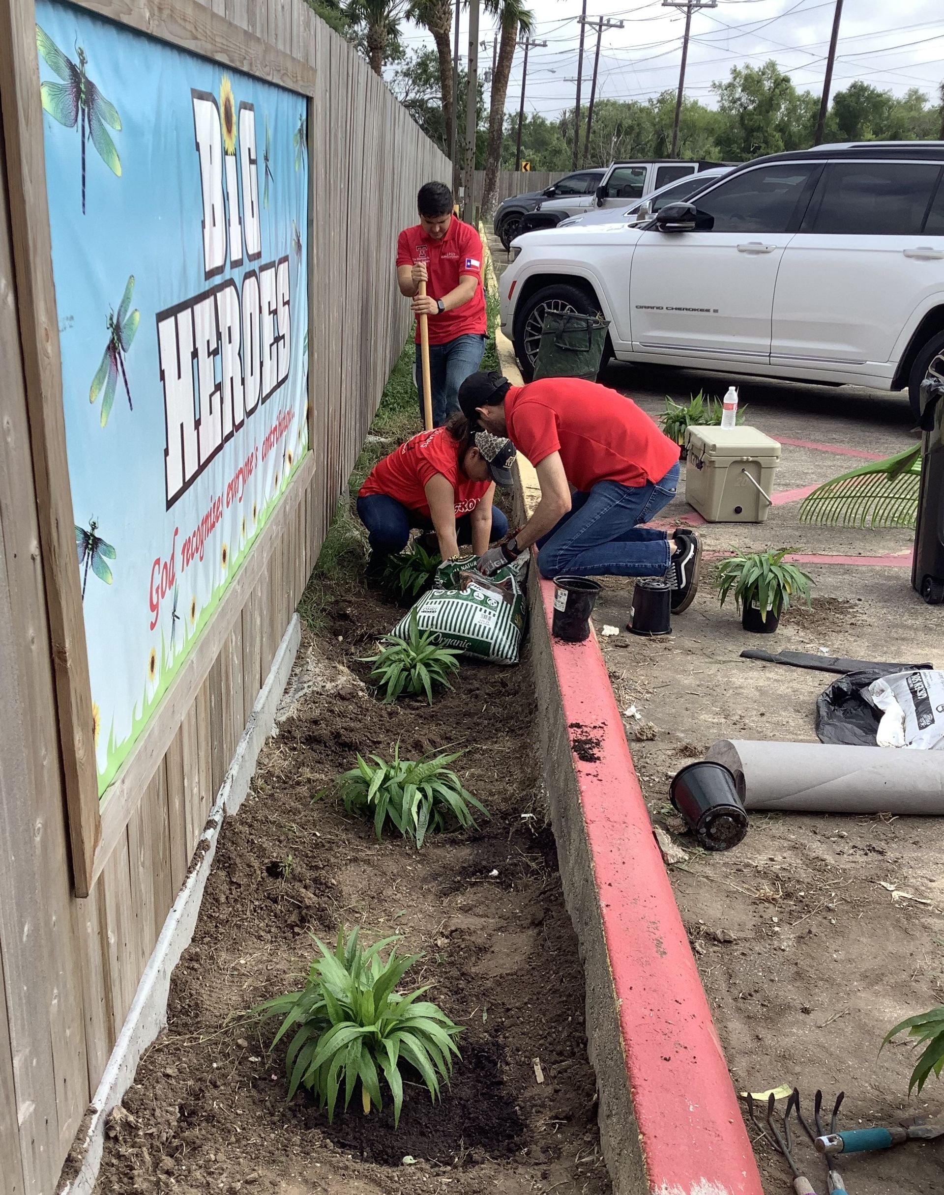 A group of people are working in a garden next to a fence.