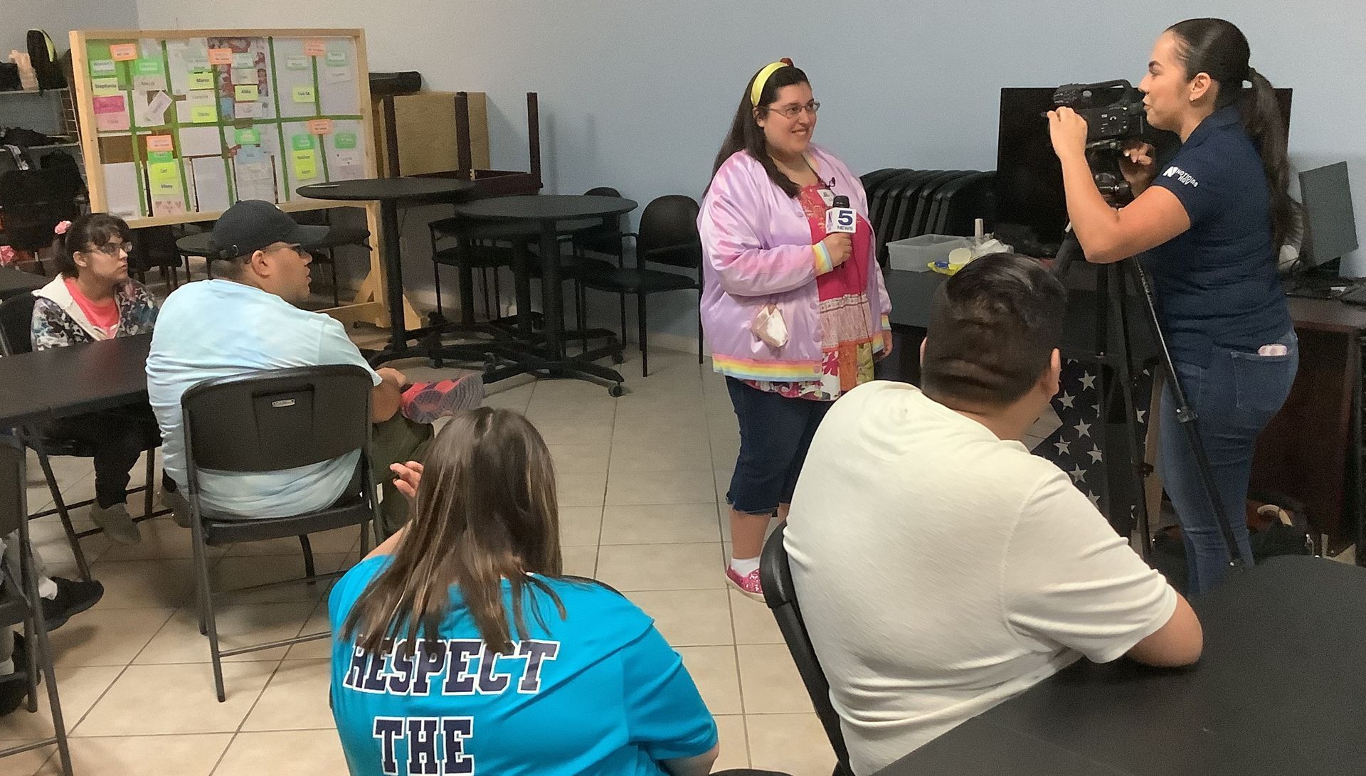 A woman is standing in front of a group of people in a room.