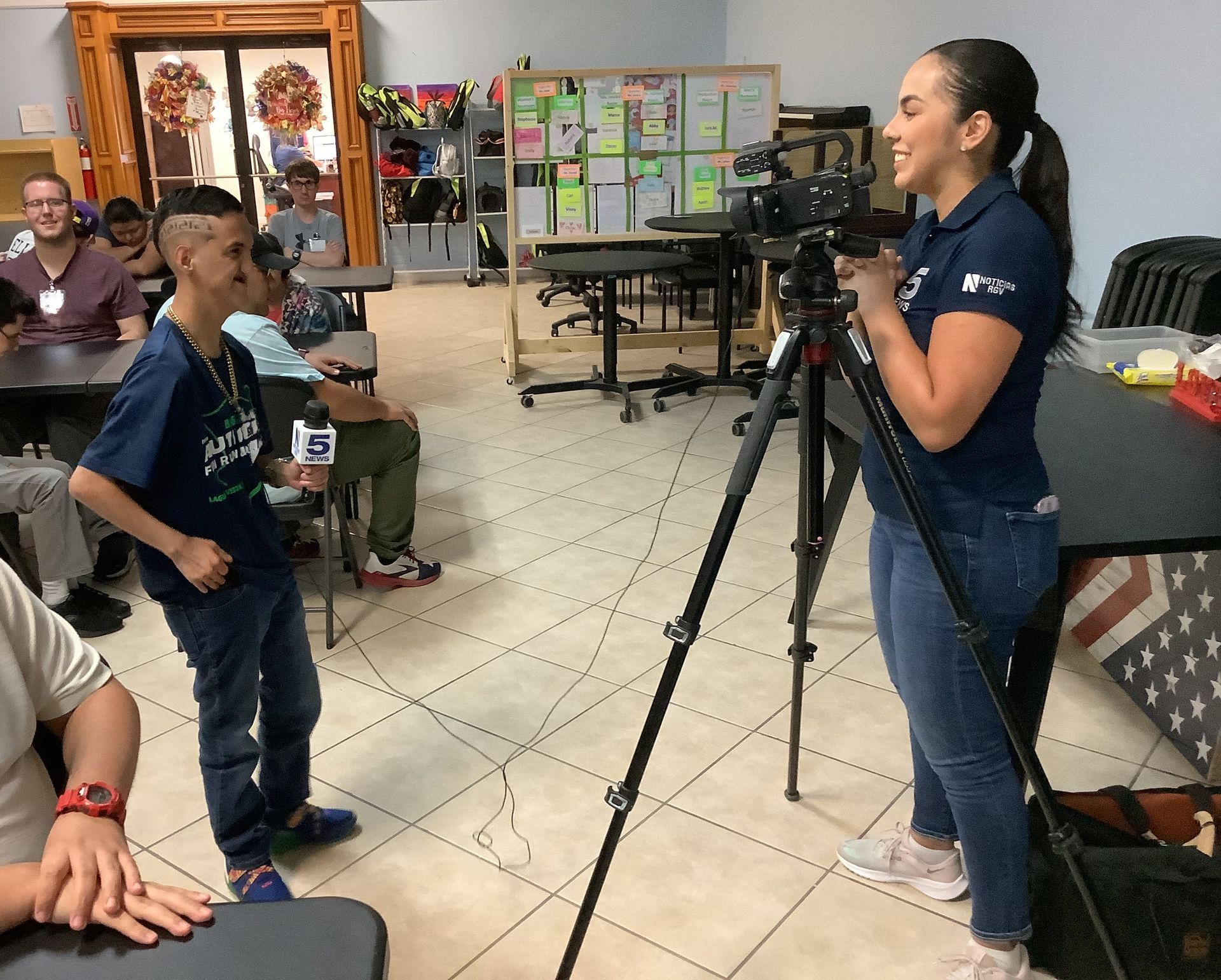 A woman is standing in front of a camera while a boy holds a microphone.