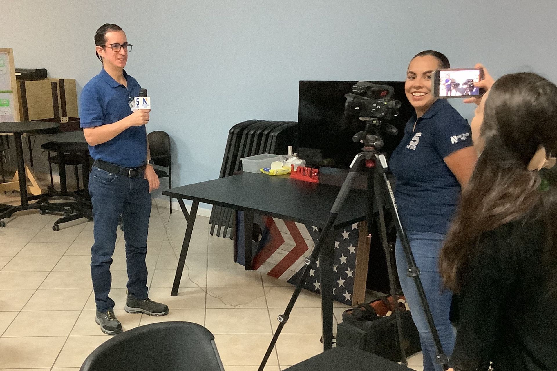 A man and a woman are standing in front of a camera in a room.