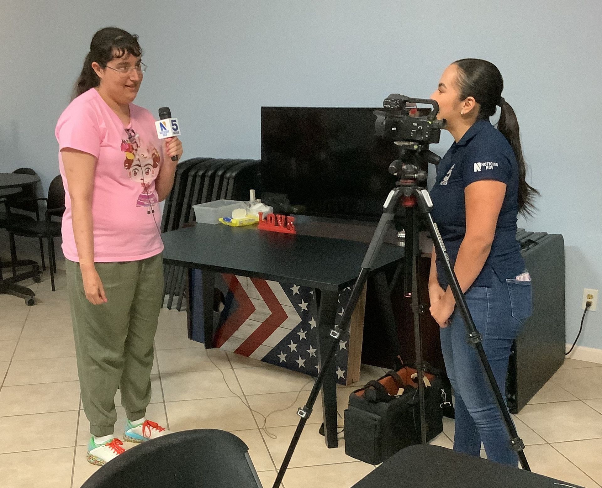 A woman in a pink shirt is talking to another woman in front of a camera