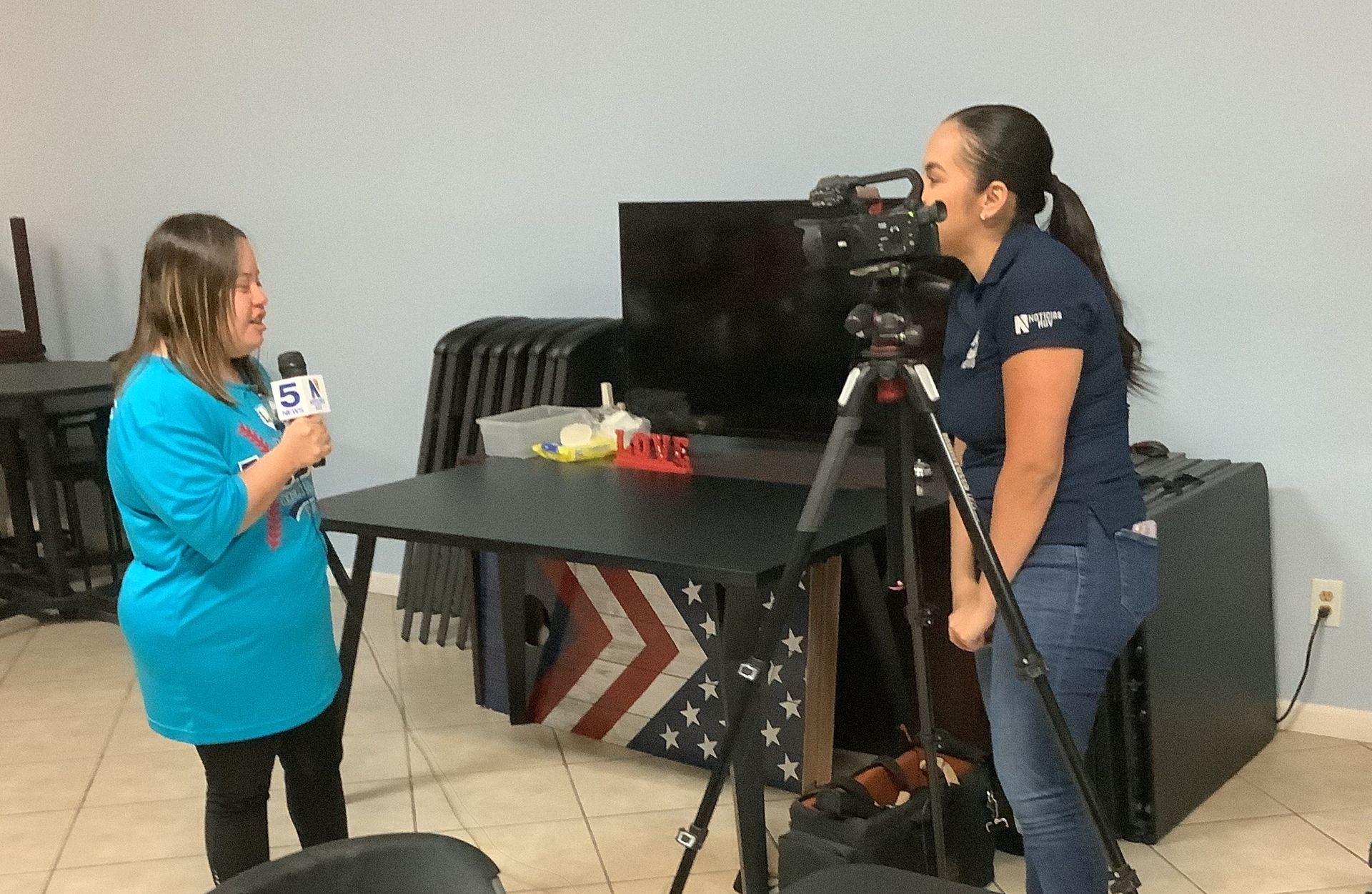 A woman is talking into a microphone while another woman stands in front of a camera.