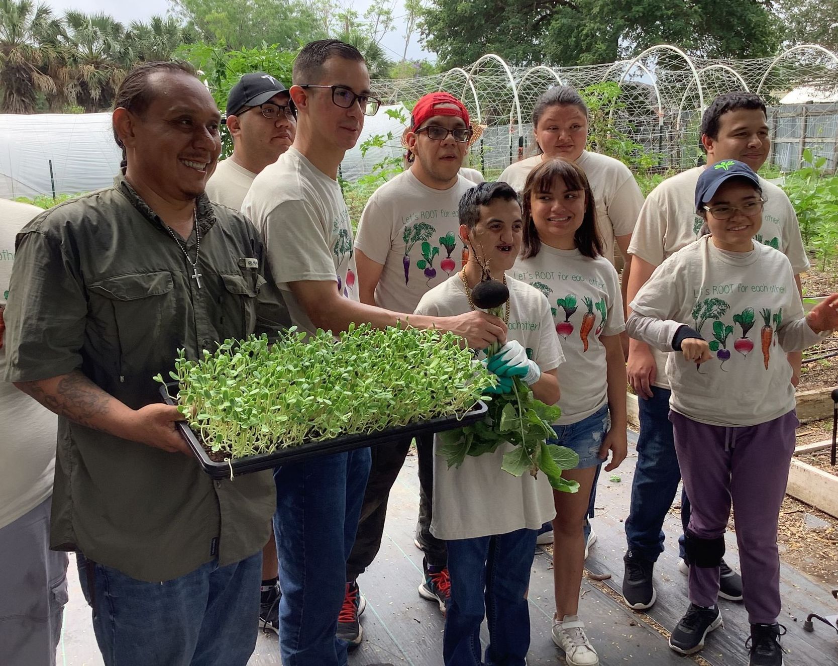 A group of people are standing around a man holding a tray of sprouts.
