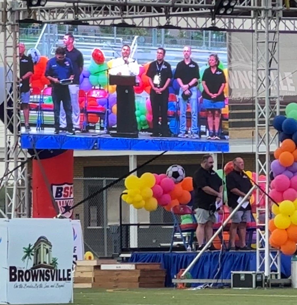 A group of people standing on a stage with balloons and a sign that says brownsville