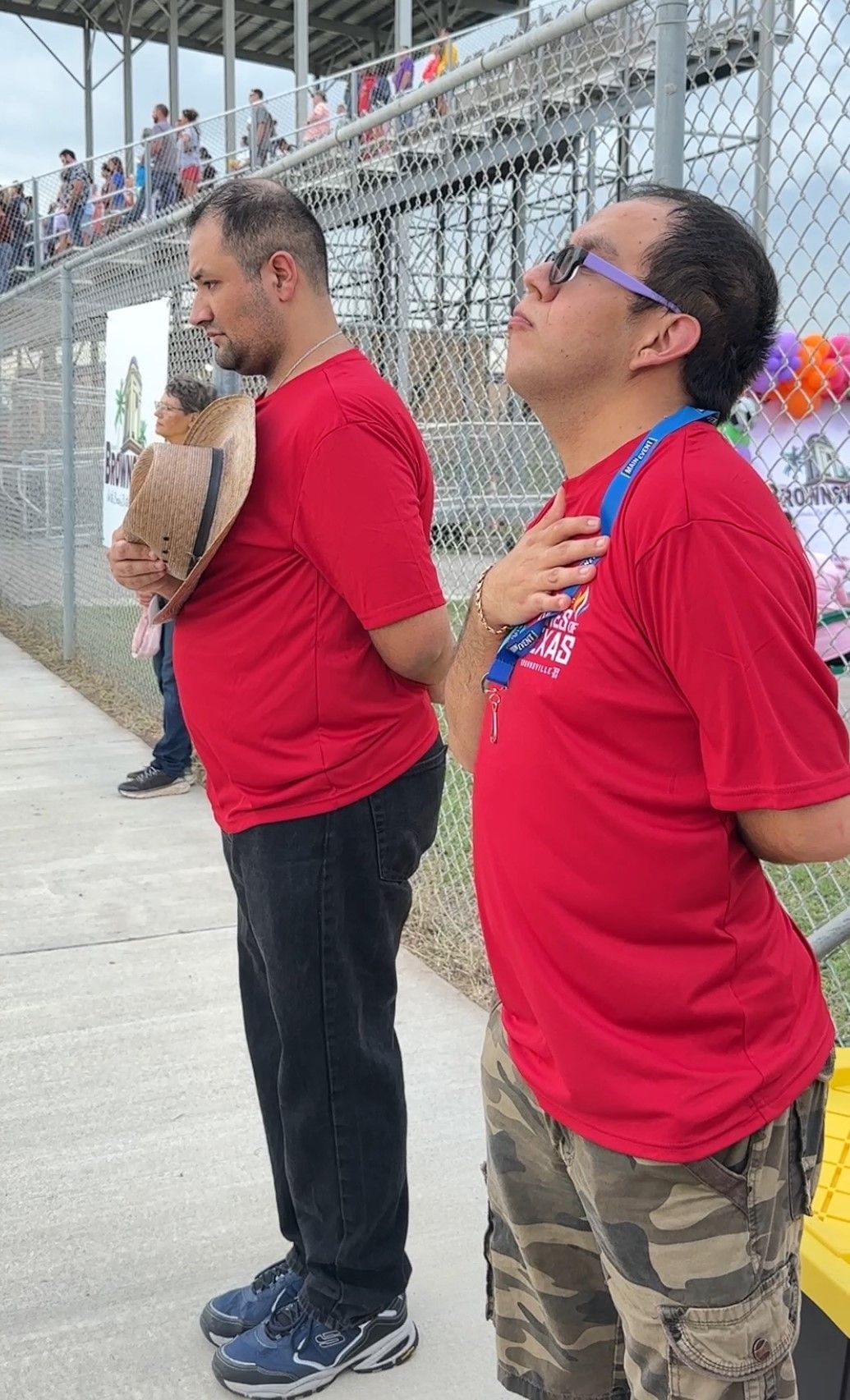 Two men in red shirts are standing next to each other on a sidewalk.