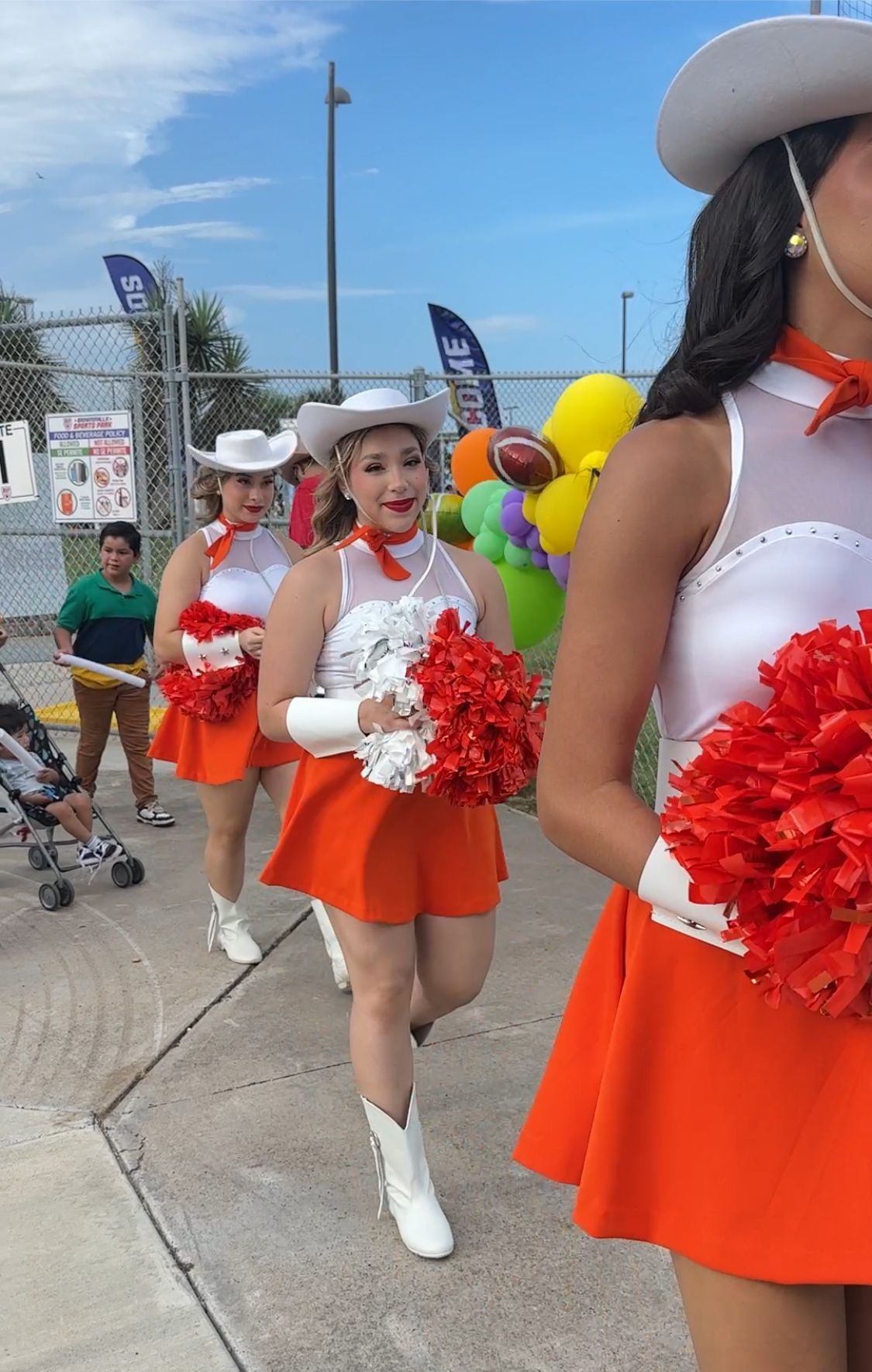 A group of cheerleaders are walking down a sidewalk holding pom poms.