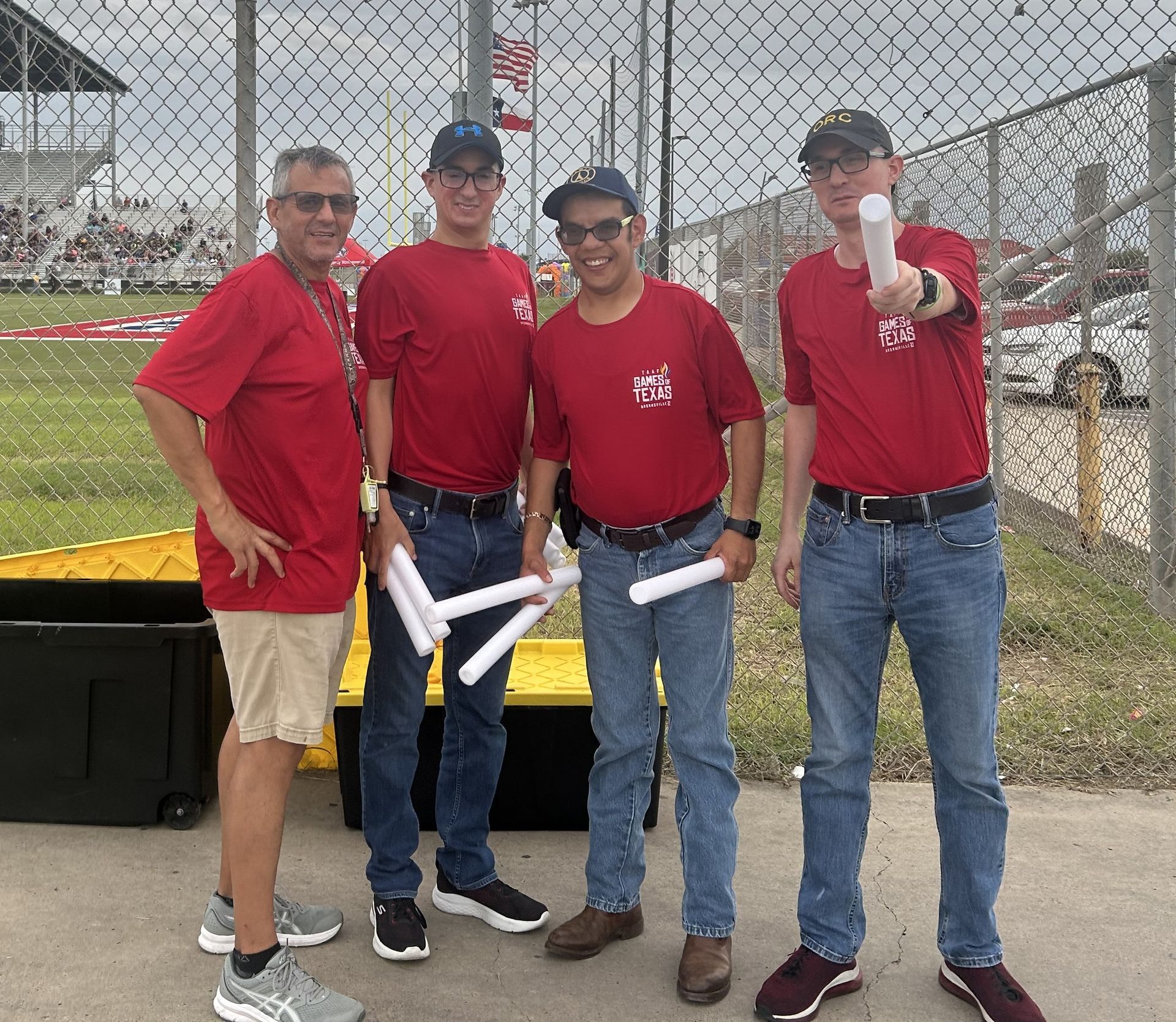 A group of men in red shirts are standing next to each other in front of a chain link fence.