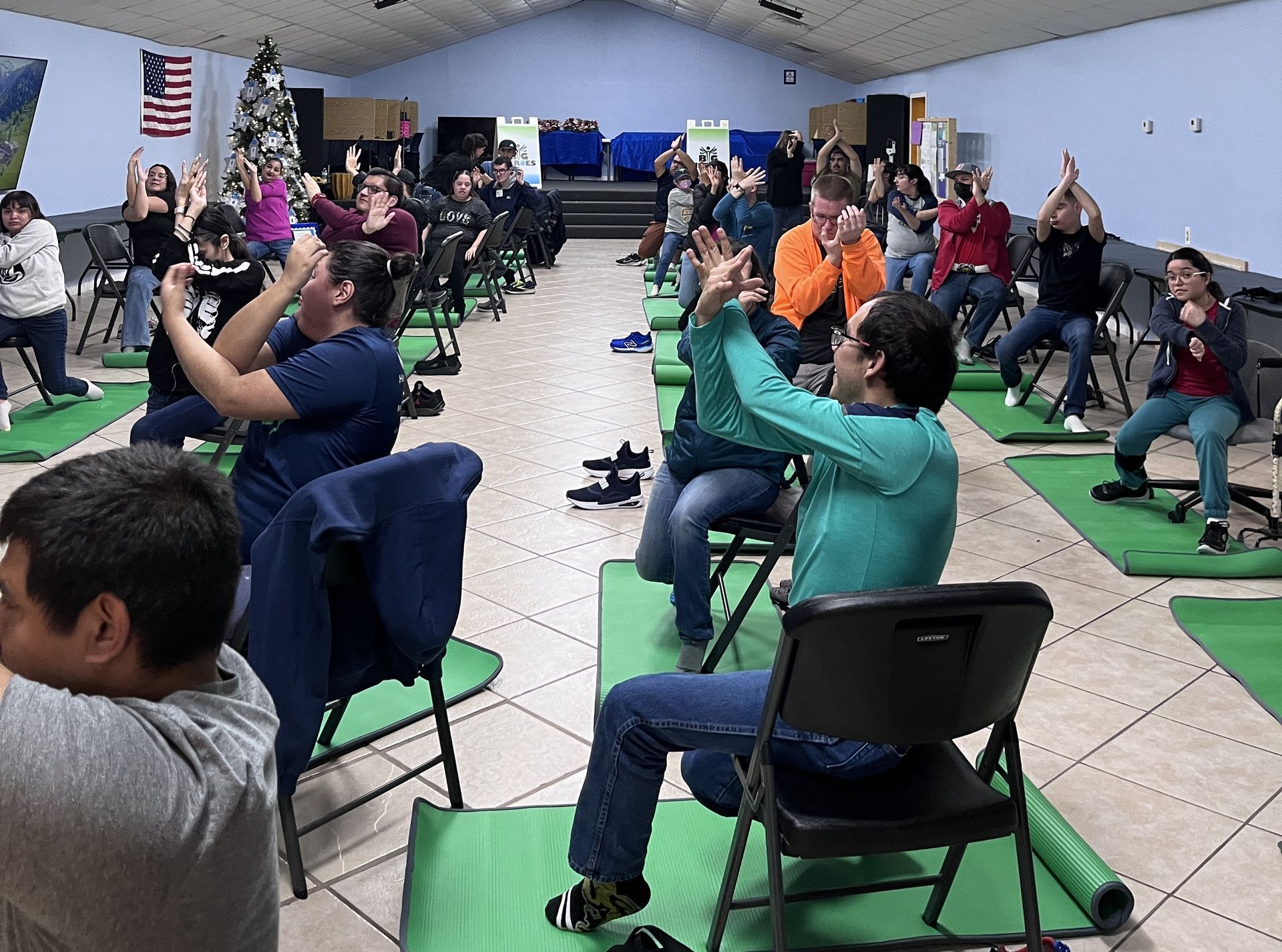 A group of people are sitting on green mats in a room