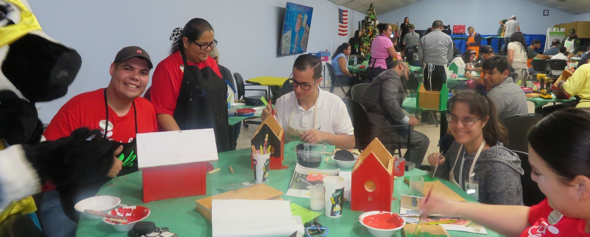 A group of people are sitting at a table painting houses.