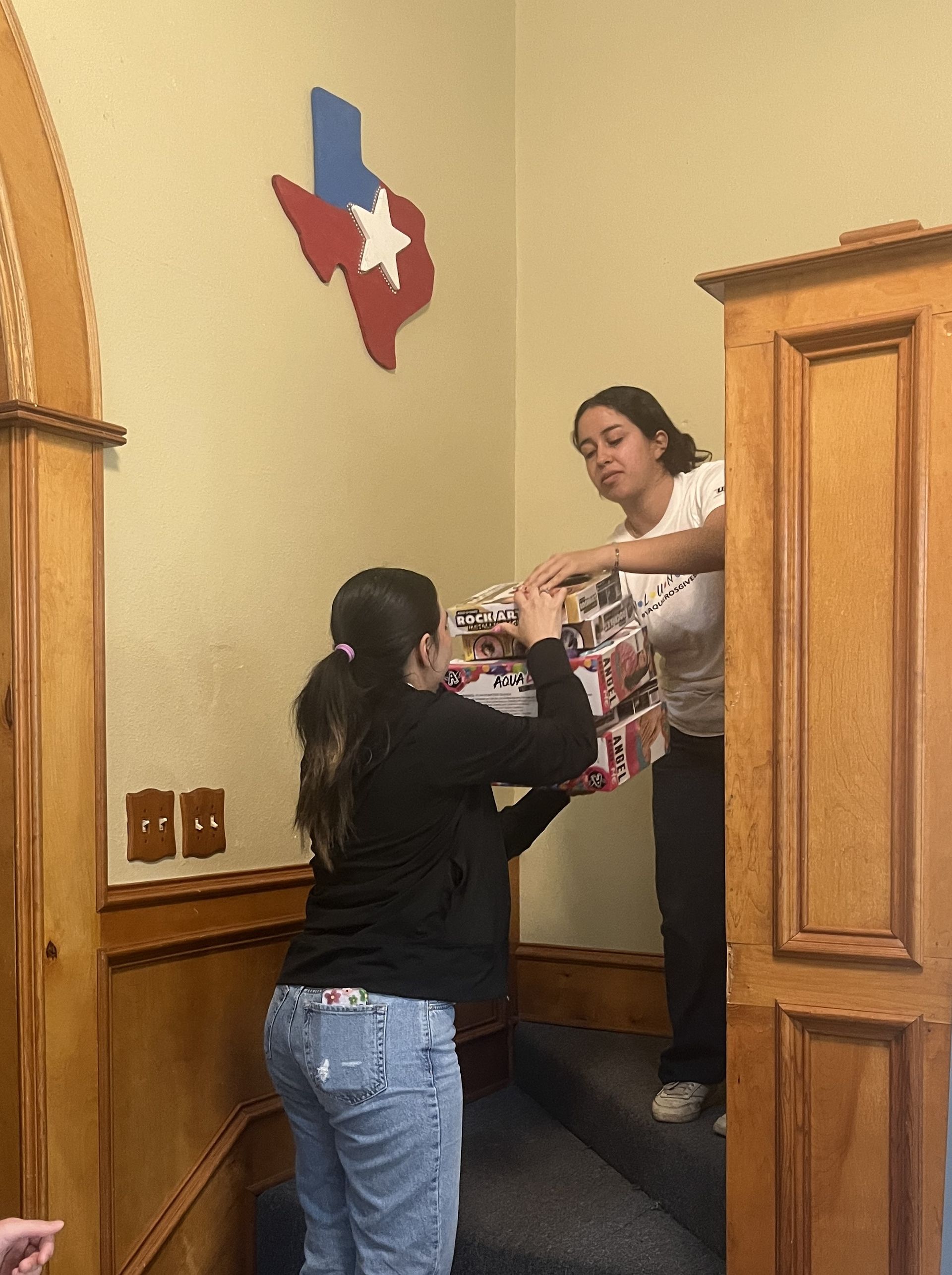 Two women are standing in a room with a texas flag on the wall.