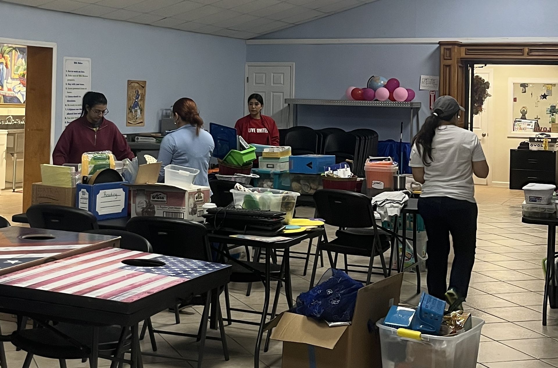 A group of people are standing in a room filled with tables and chairs.