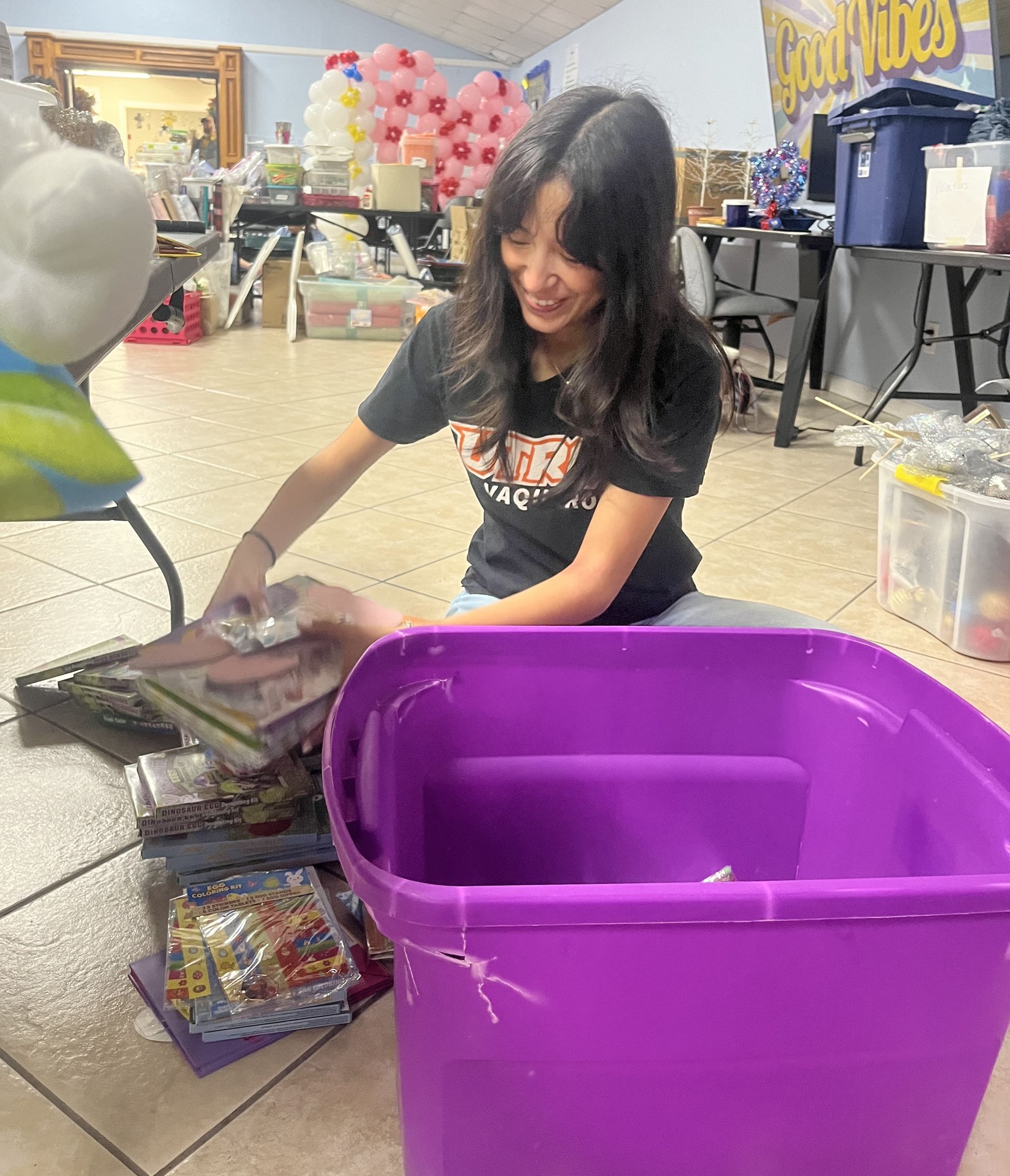 A woman is sitting on the floor next to a purple bin.