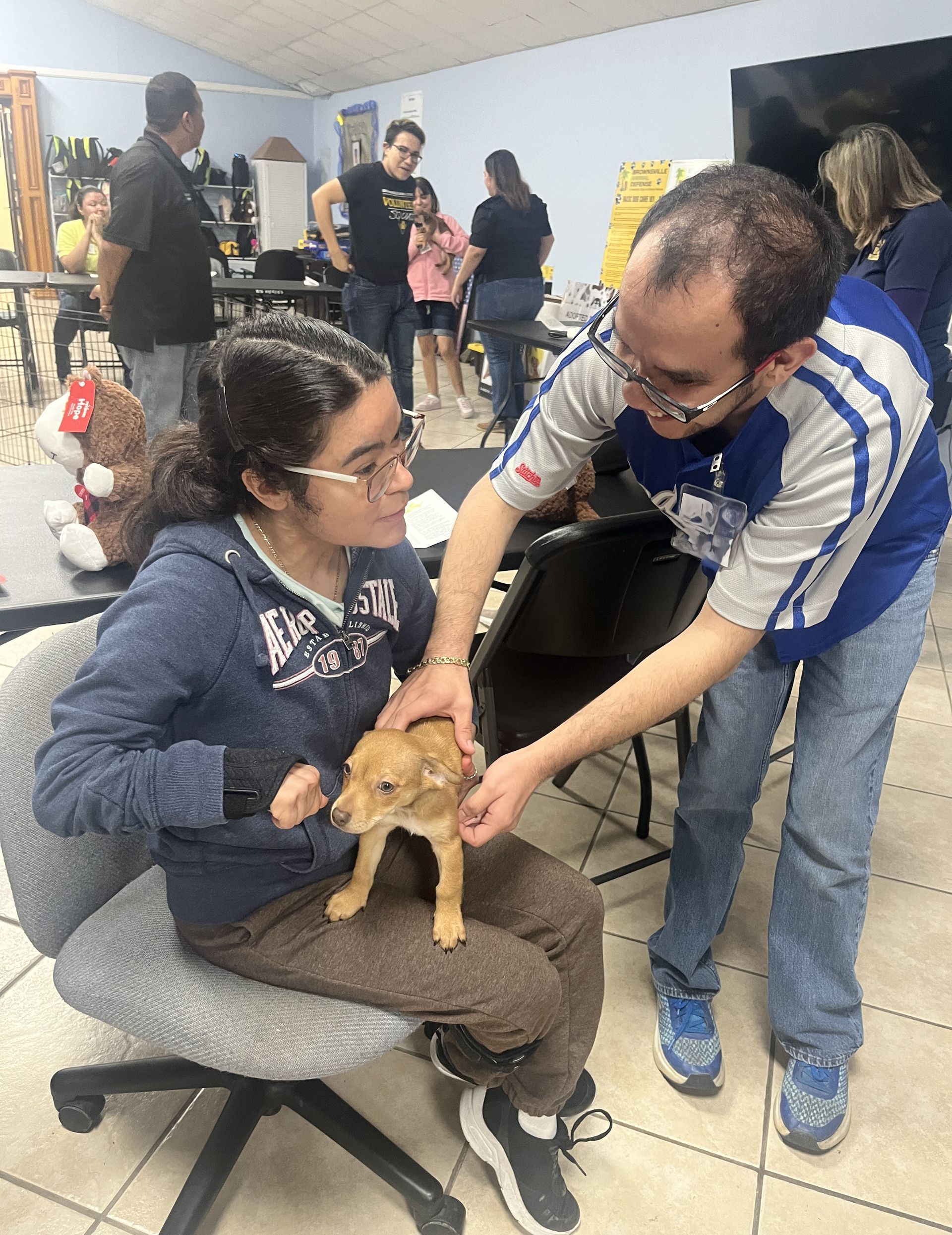 A man is petting a puppy while a girl sits in a chair.