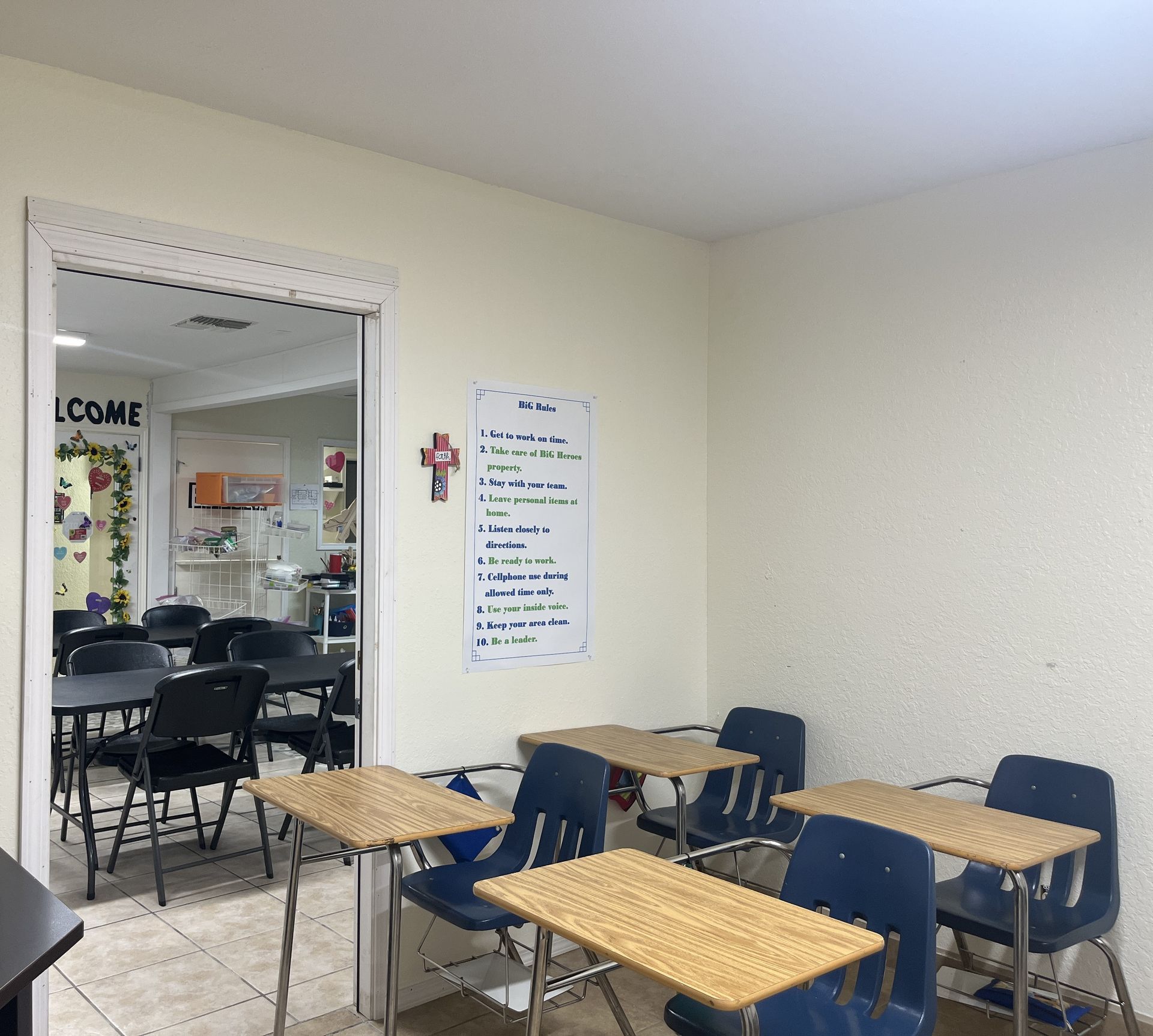 A classroom with tables and chairs and a cross on the wall.