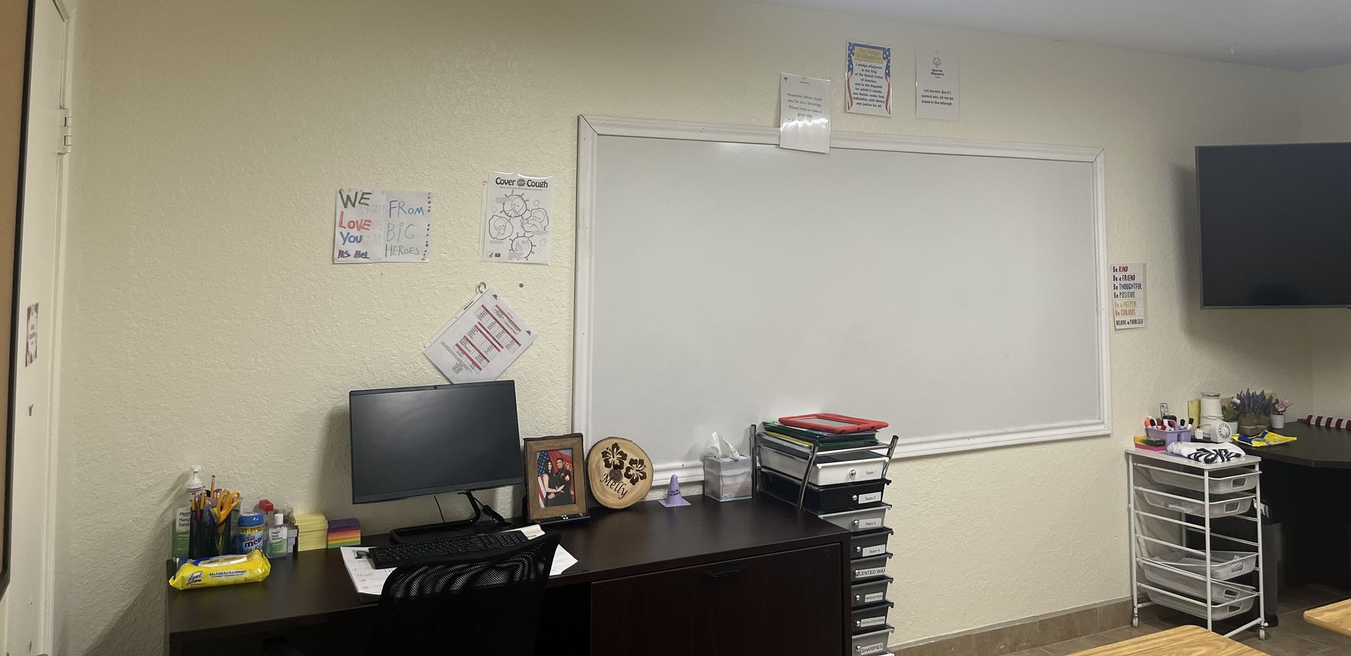 A desk with a computer and a whiteboard in a room.