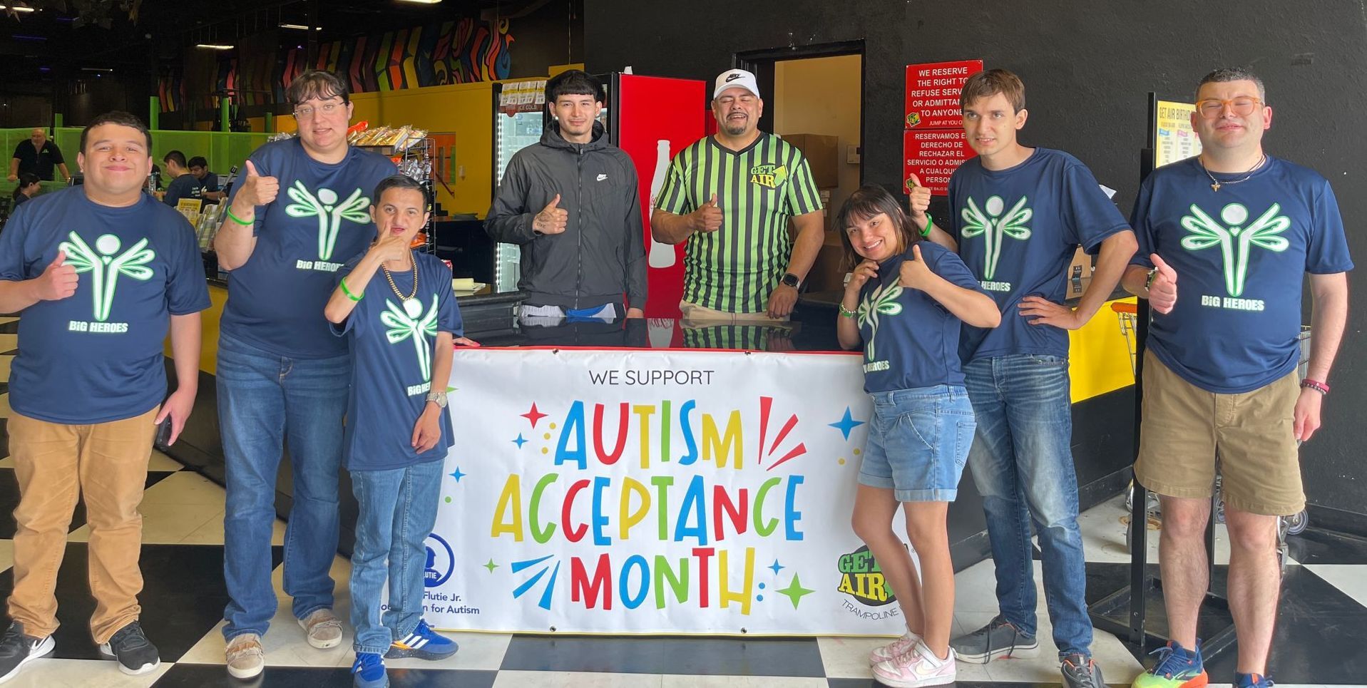 A group of people standing next to each other in front of a sign that says autism acceptance month.
