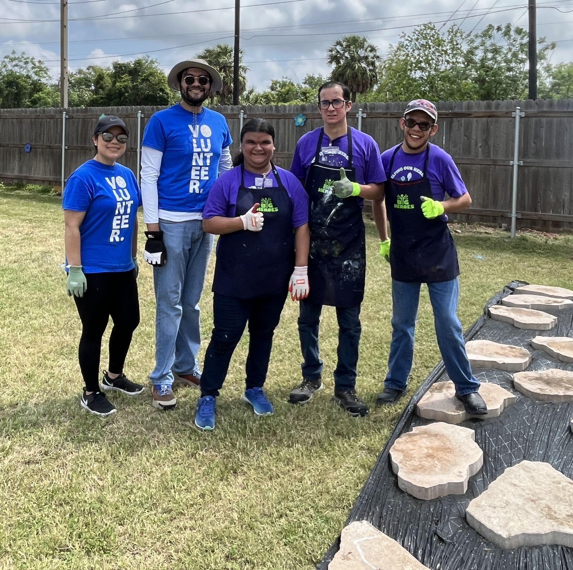 A group of people standing in a grassy field wearing blue shirts that say volunteer