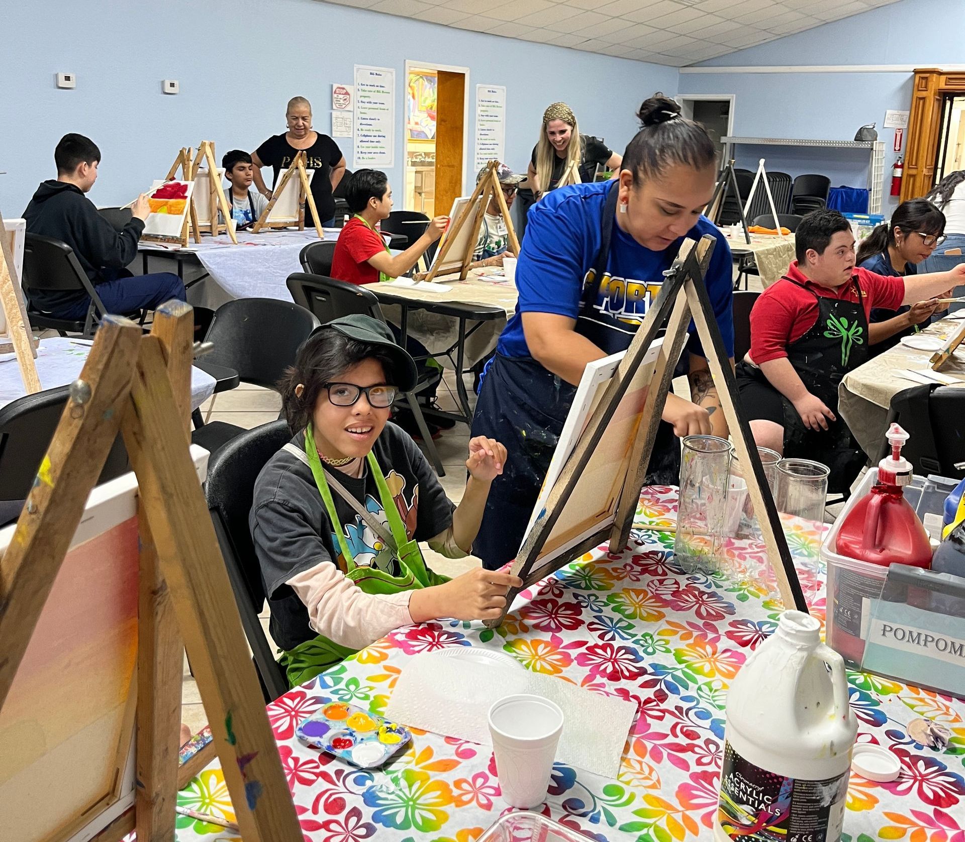 A group of people are sitting at tables painting on canvases.