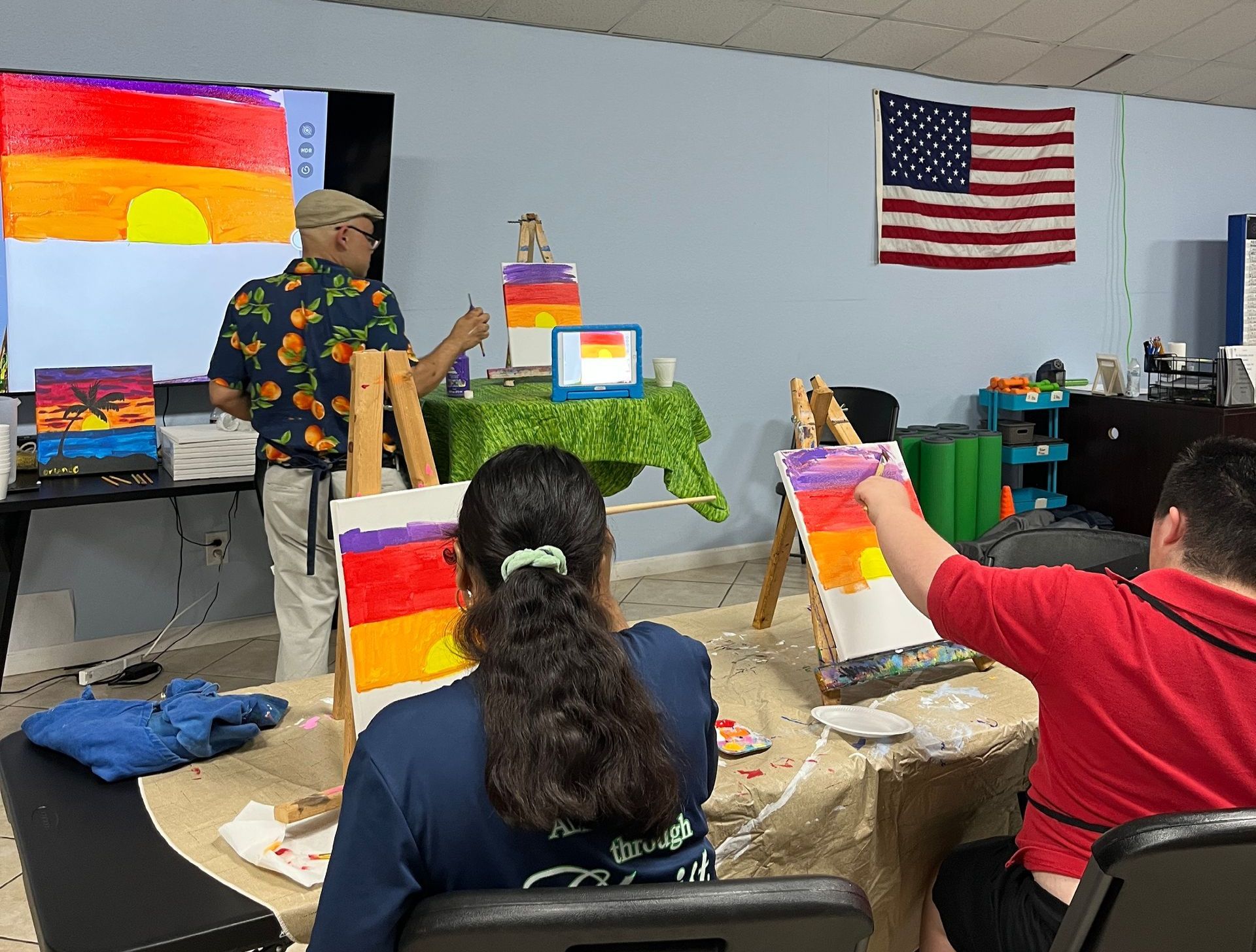 A man is teaching a group of people how to paint on an easel.