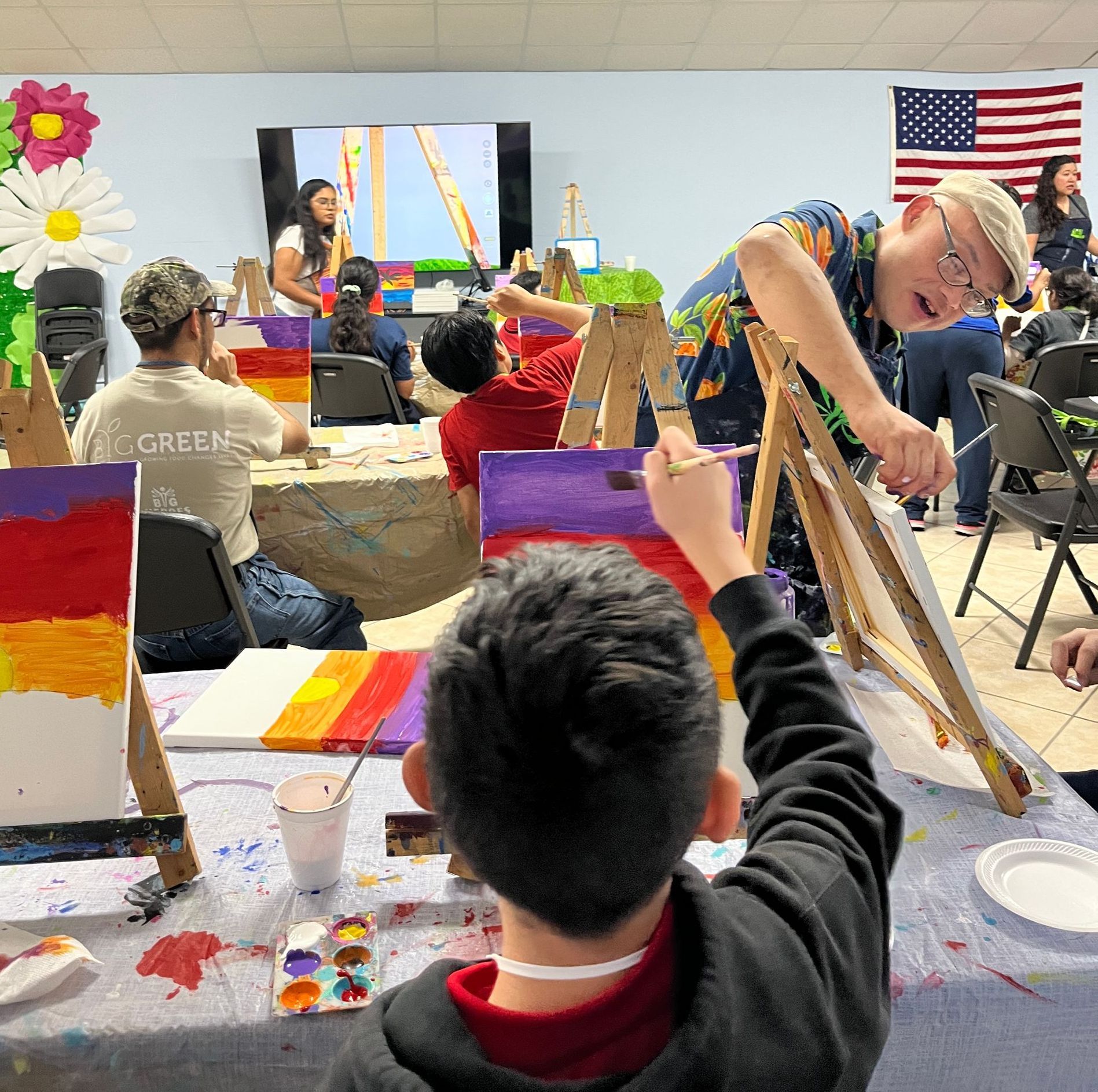 A group of people are painting in a room with an american flag in the background