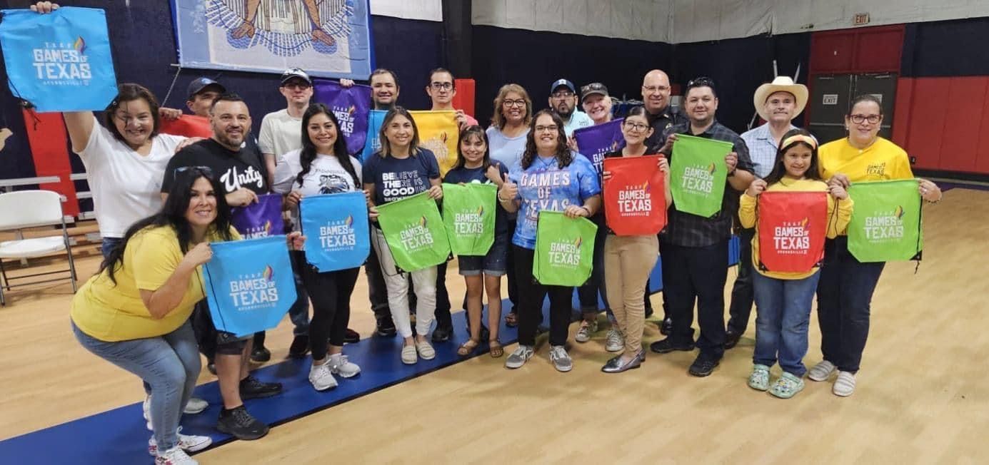 A group of people are standing in a gym holding bags.