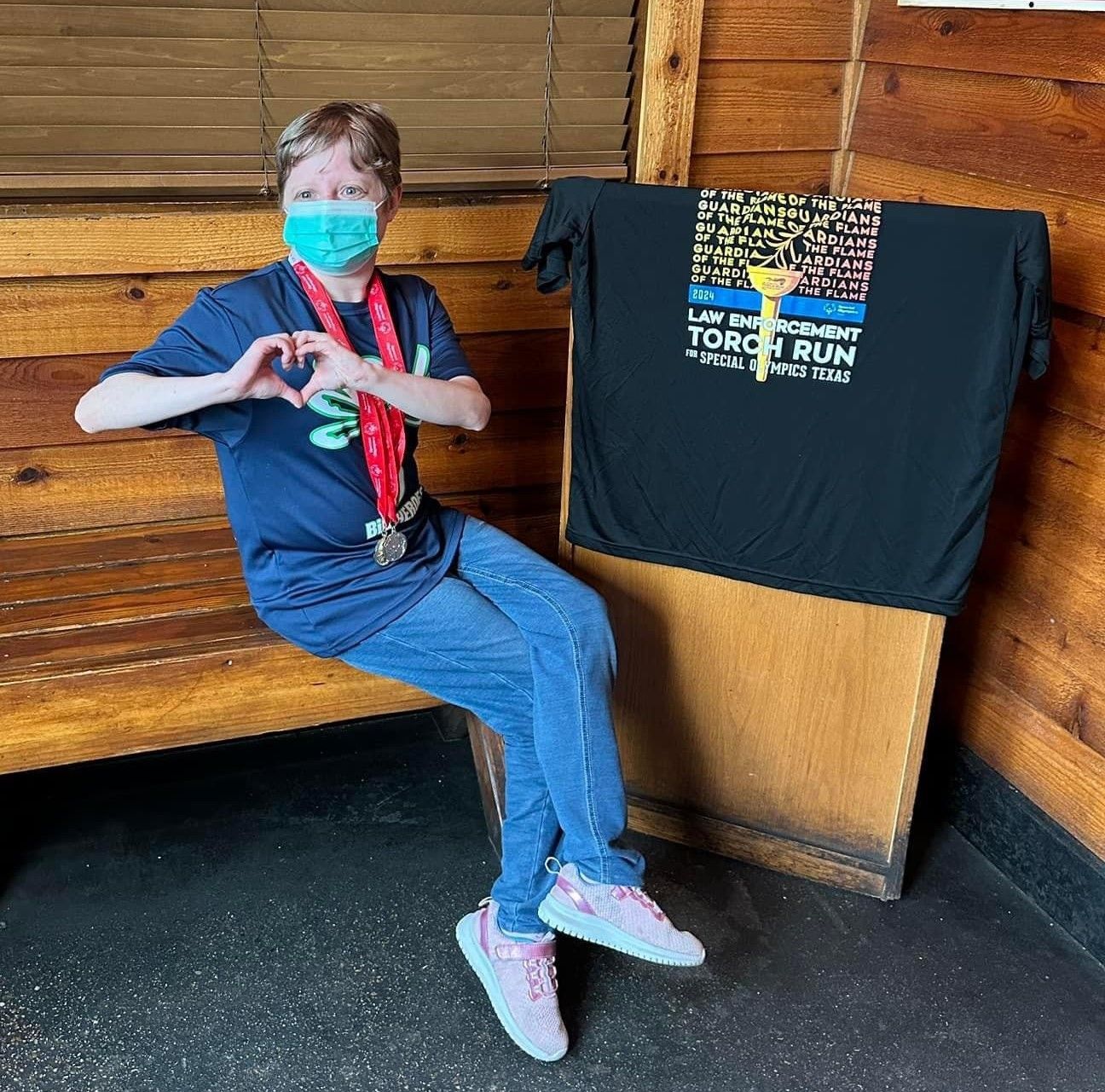 A woman wearing a mask is sitting on a bench next to a torch run shirt